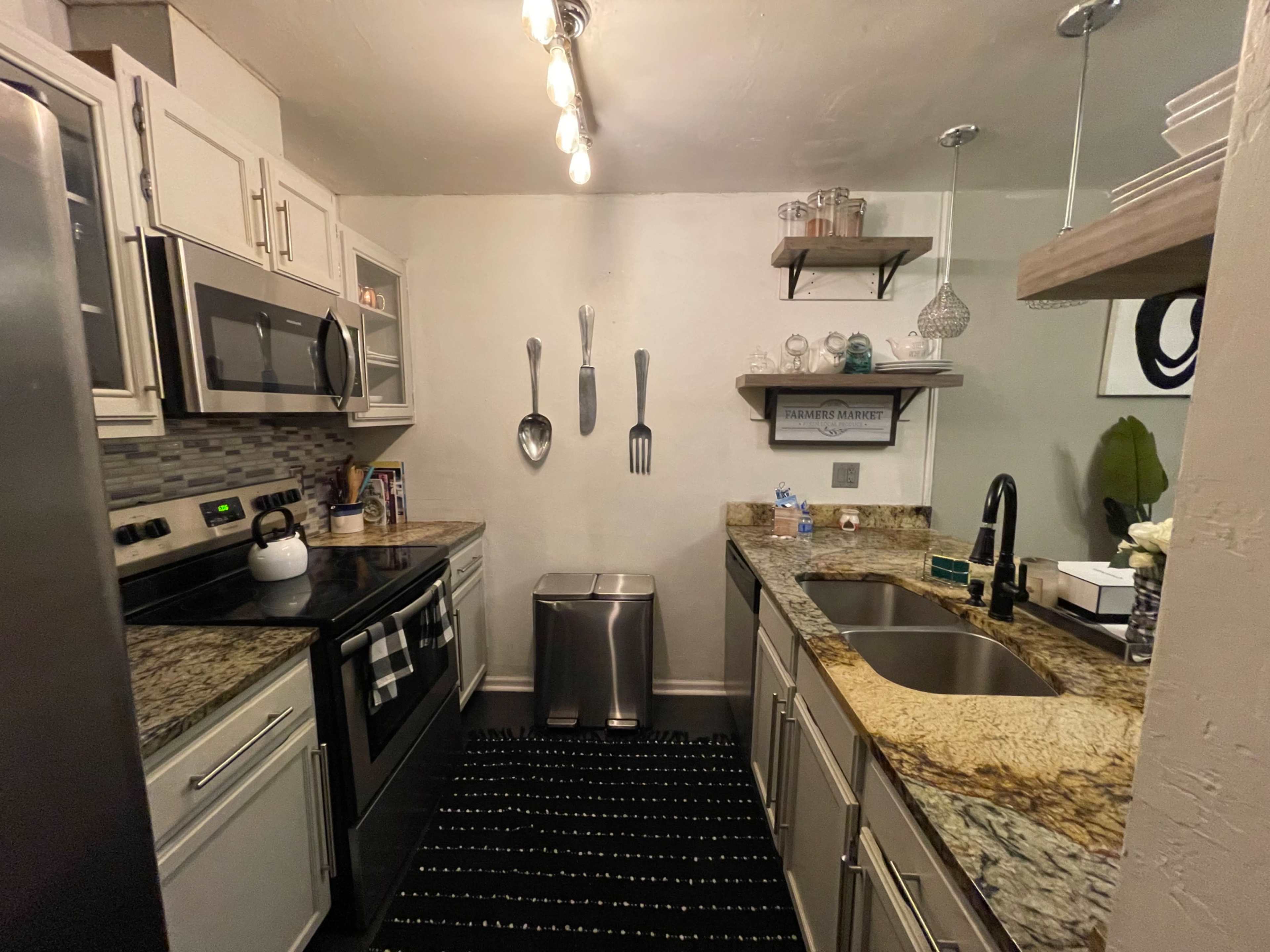 A compact kitchen with stainless steel appliances, granite countertops, and decorative utensils mounted on the wall.