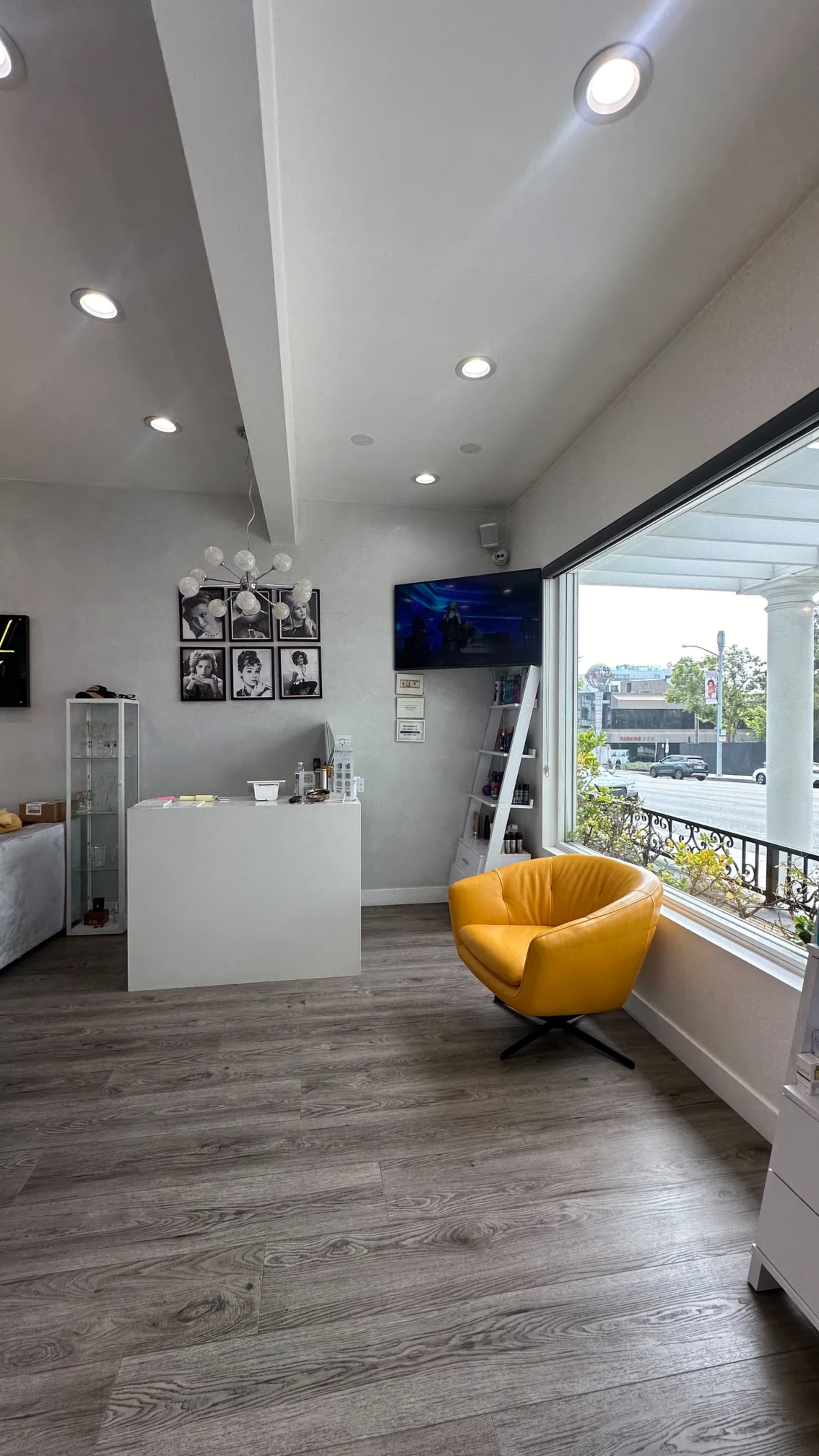The interior of a modern salon features a bright yellow chair, a reception desk, and large windows overlooking an outdoor view.