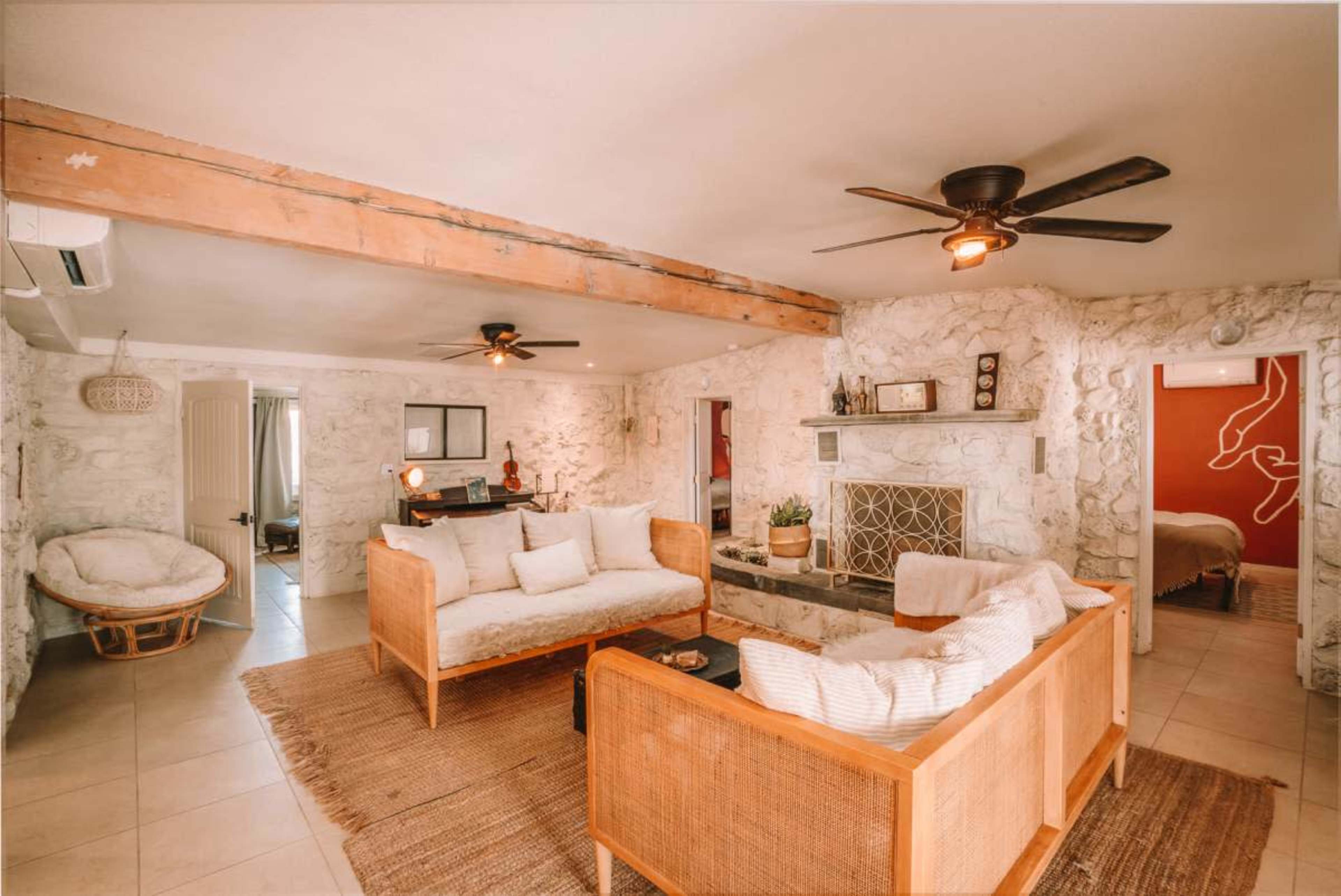 The room features a cozy living area with two wooden-framed sofas, a stone wall, and an open layout that connects to other spaces.