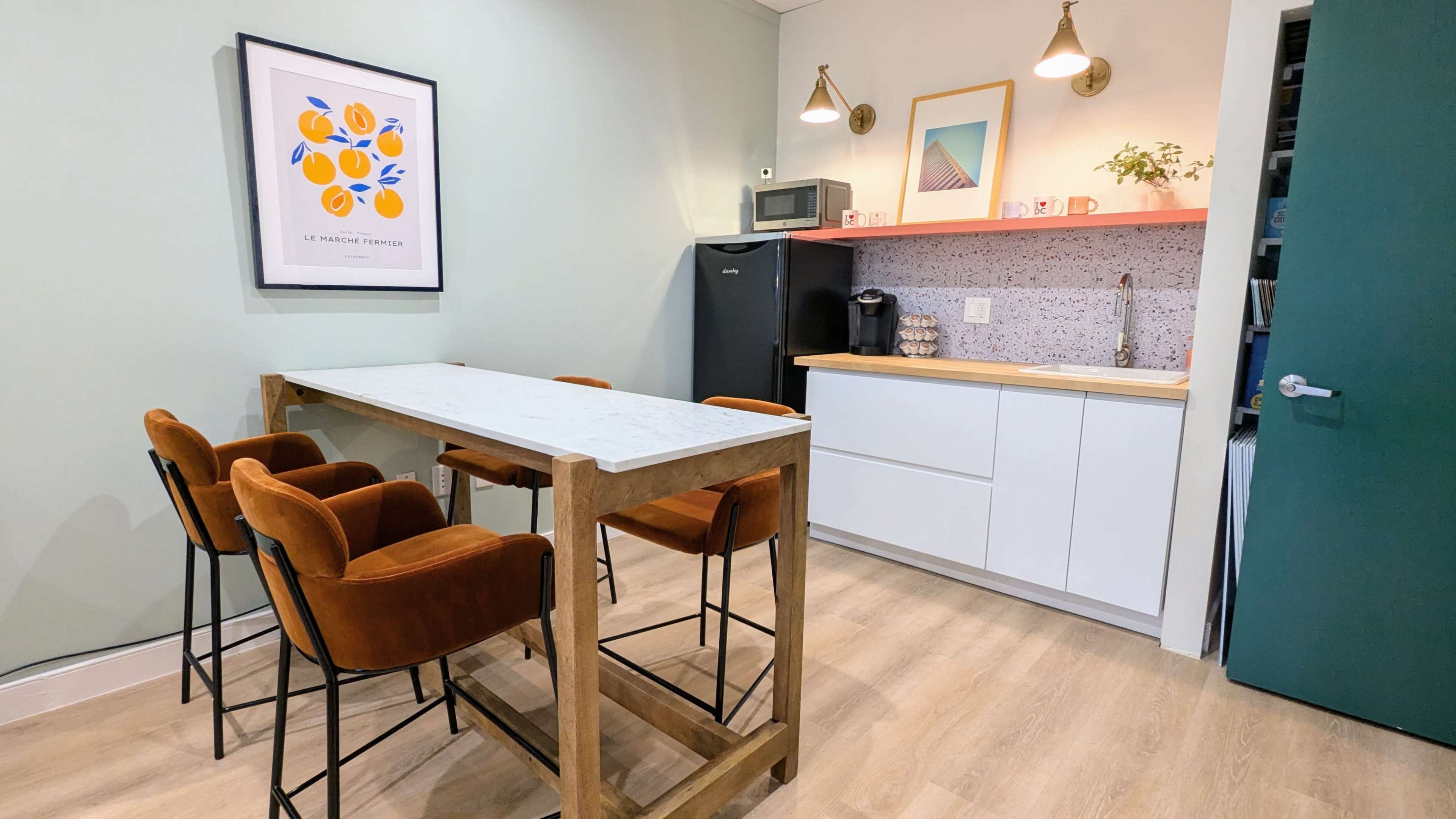 A kitchen area features a marble-topped table with four upholstered chairs, a black refrigerator, and a countertop adorned with a backsplash and various kitchen appliances.