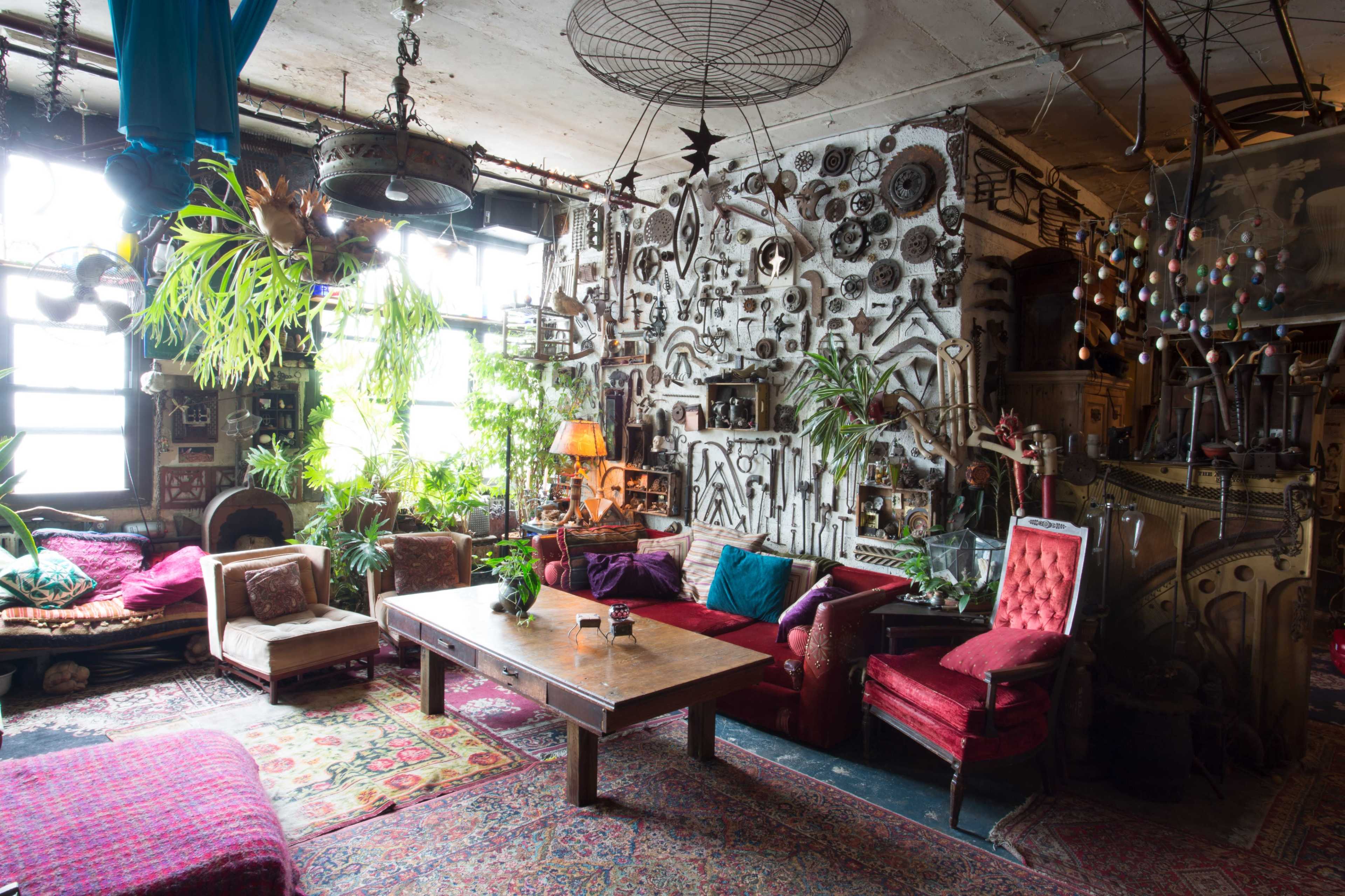 A vintage-style living room filled with eclectic decor, plants, and colorful furniture arranged around a wooden table.