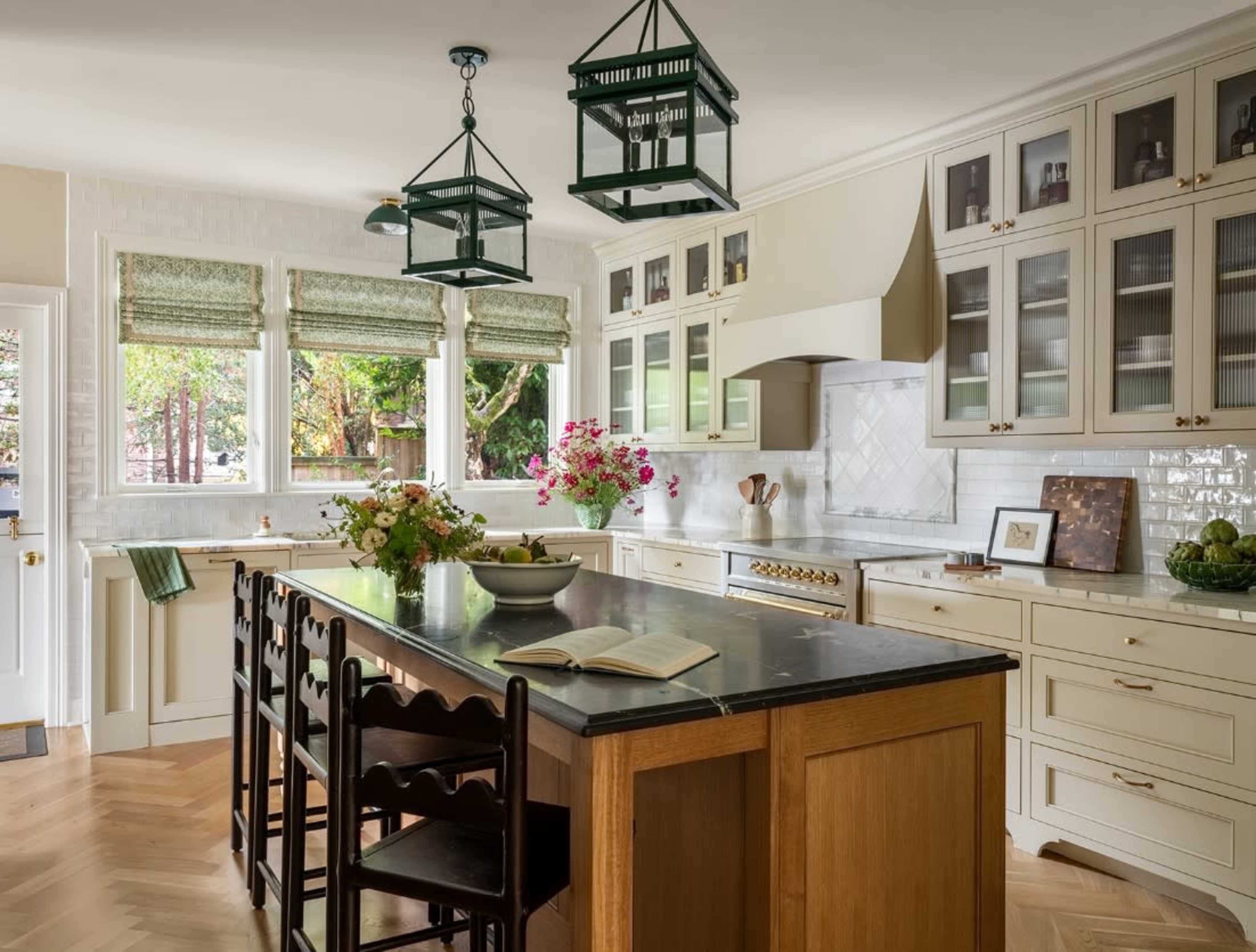 The kitchen features a large central island with wooden cabinetry, white countertops, and glass-fronted cupboards, all enhanced by natural light from the windows.