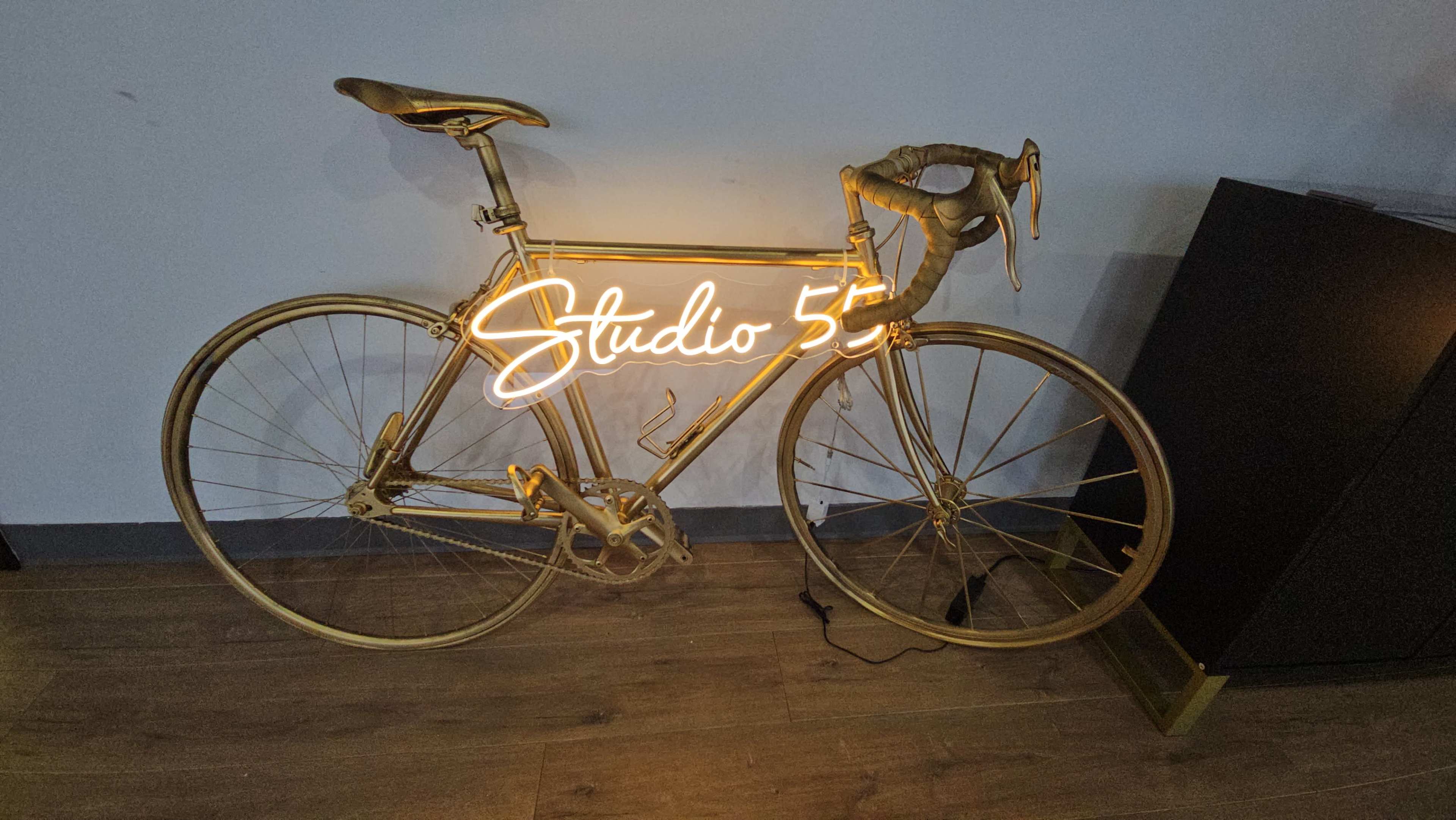 A gold-painted bicycle is propped against a wall with a neon sign reading "Studio 5" illuminated above it.