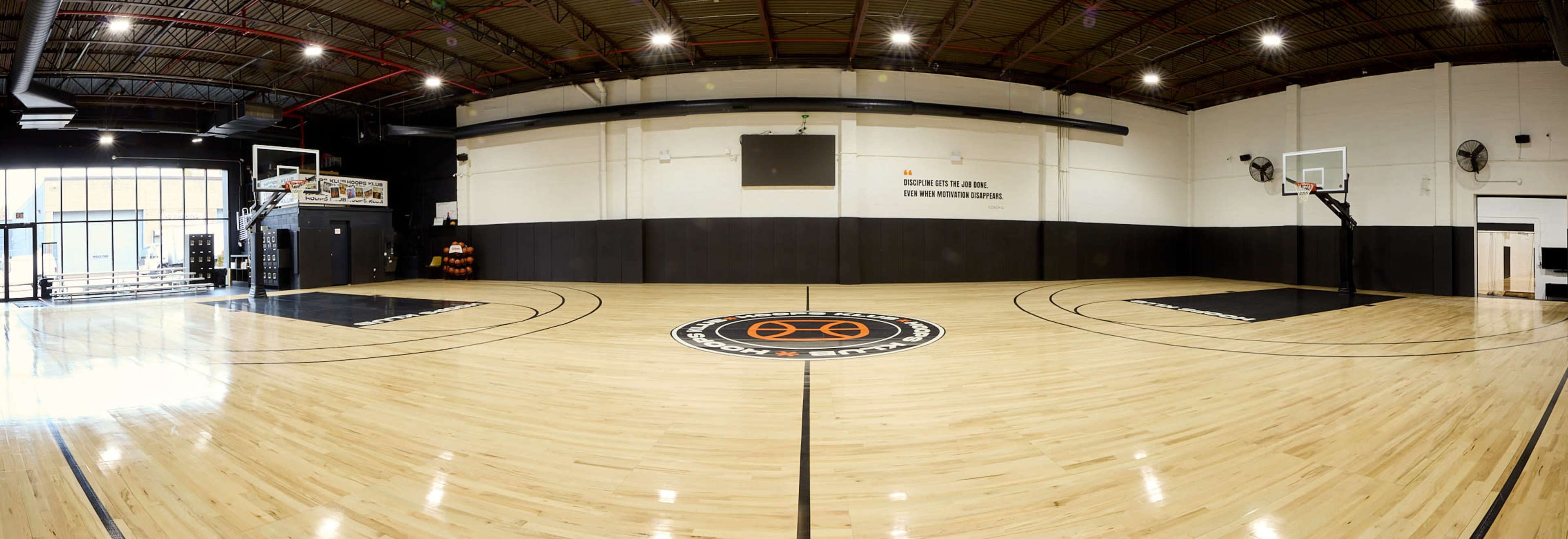 The image shows a panoramic view of a basketball court with wooden floors, marked lines, and basketball hoops at each end.