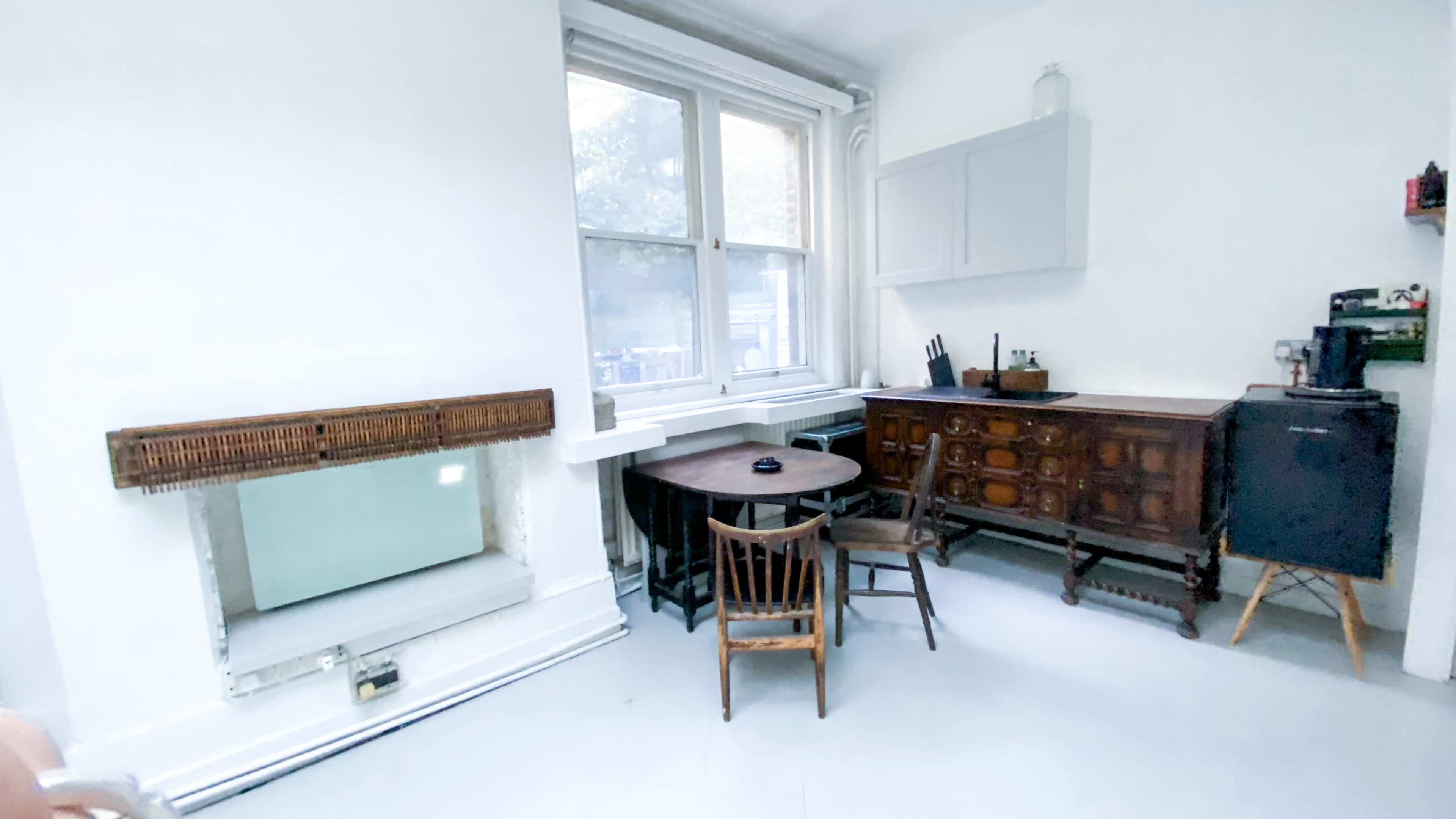 A minimalist kitchen with a wooden dining table, a few chairs, and cabinetry against the wall.