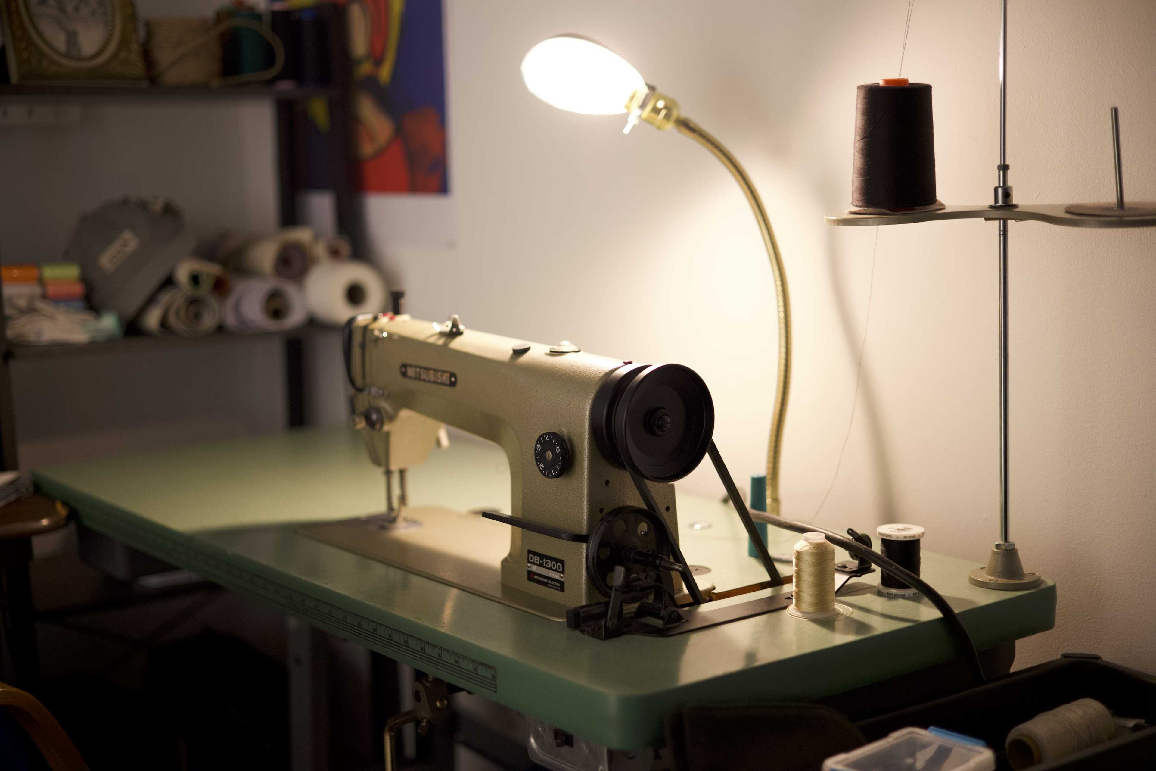 A vintage sewing machine is positioned on a green table beneath a lamp, with spools of thread and sewing supplies arranged nearby.