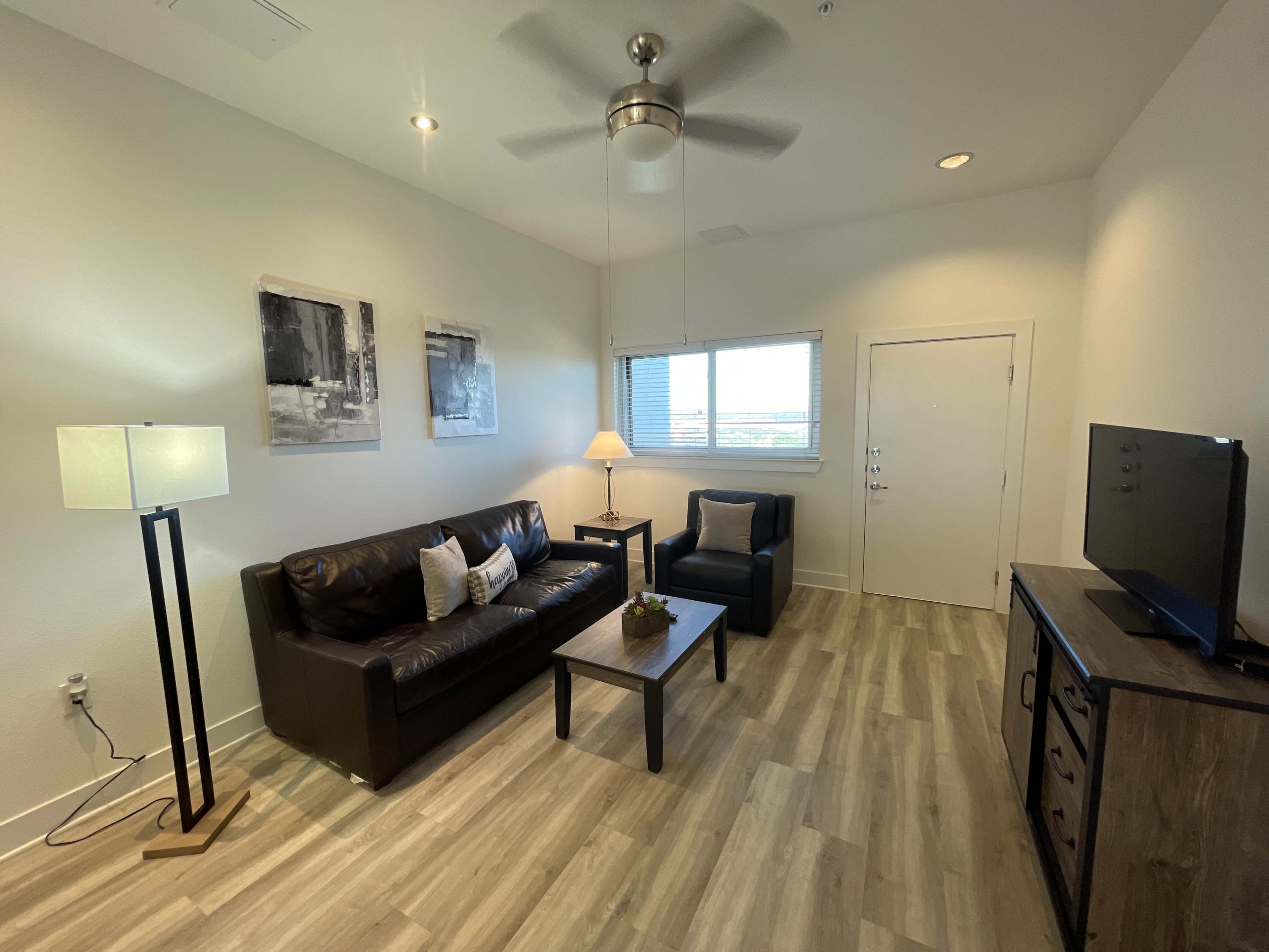A modern living room with a sofa, armchair, coffee table, lamp, and television against a light-colored wall.