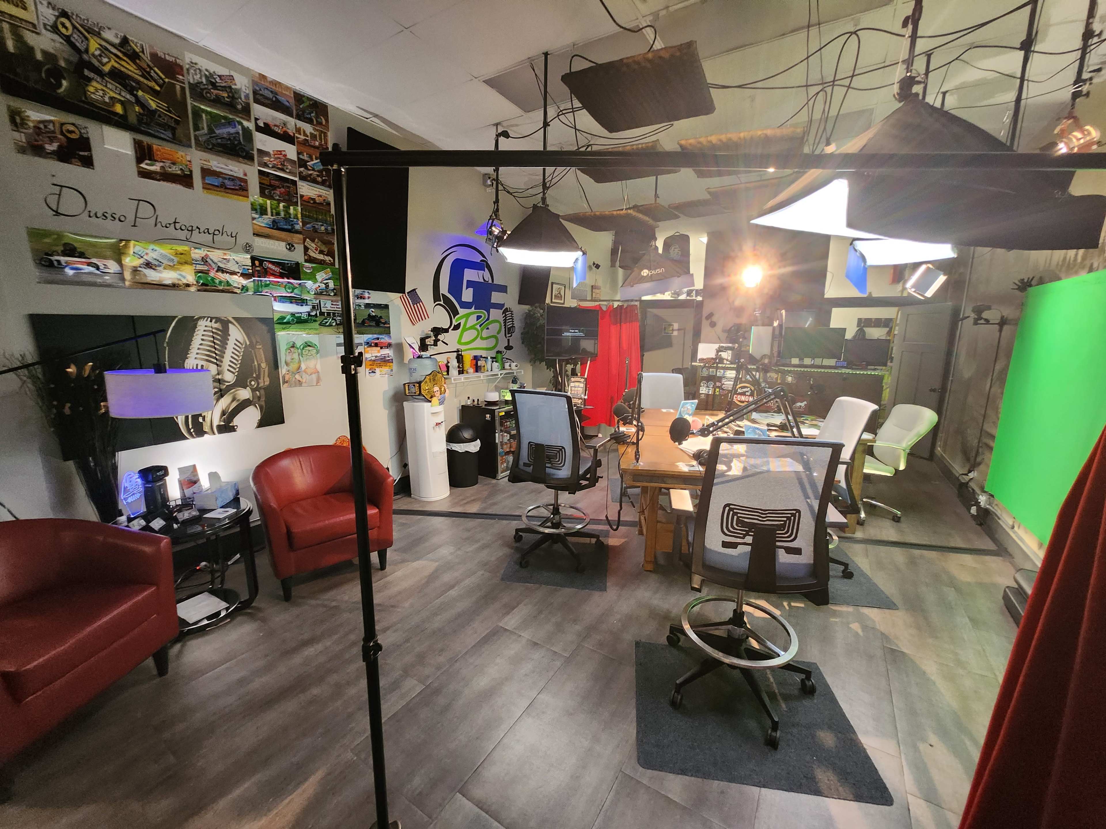 A studio space featuring red chairs, a table, green and white screens, and various photography equipment arranged around it.