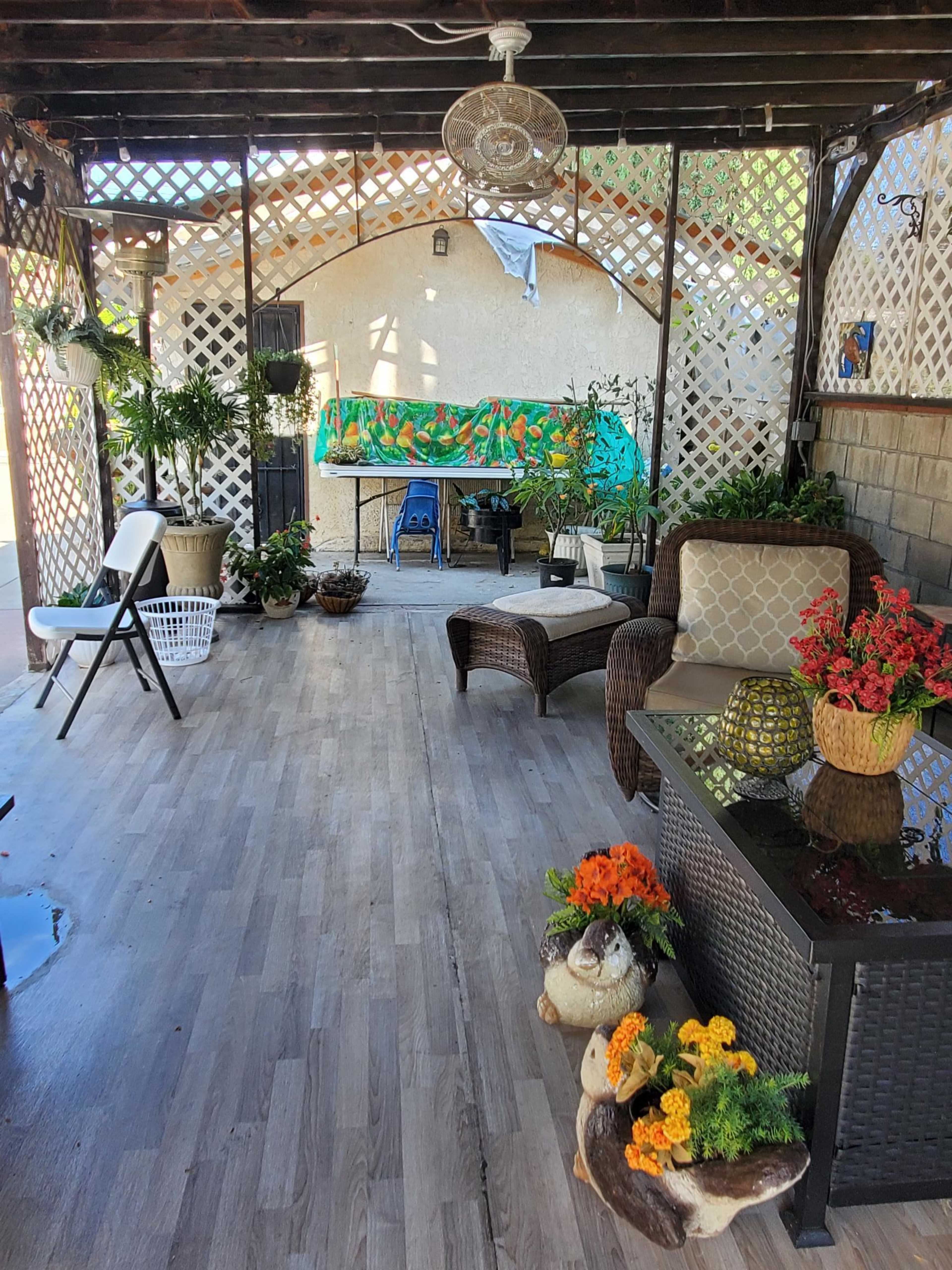 The image shows a decorated outdoor patio area with wicker furniture, plants, and a table covered in a colorful cloth, surrounded by a lattice frame.