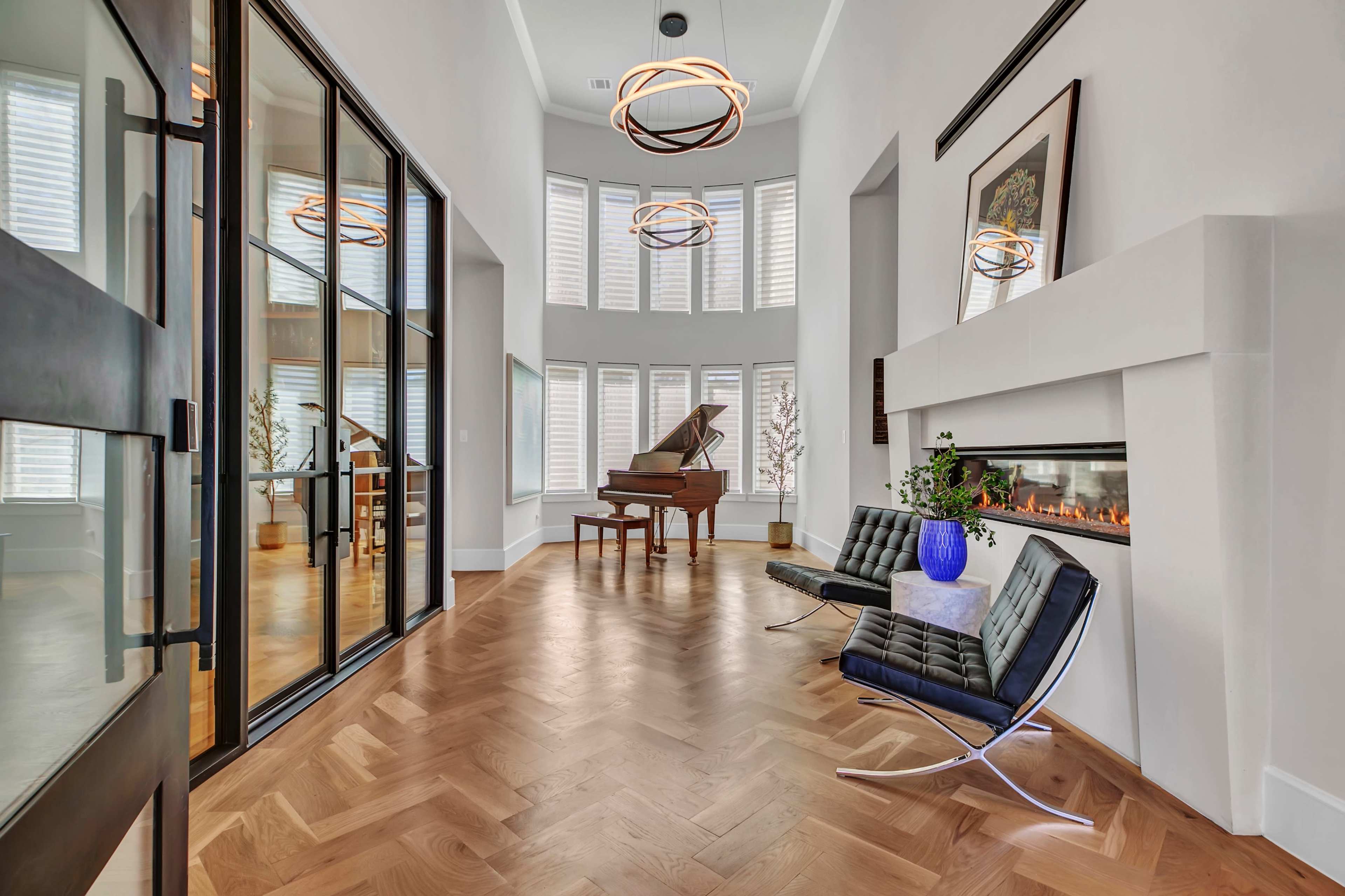 A modern interior features a grand piano, sleek seating, and a fireplace, with large windows allowing natural light to fill the space.