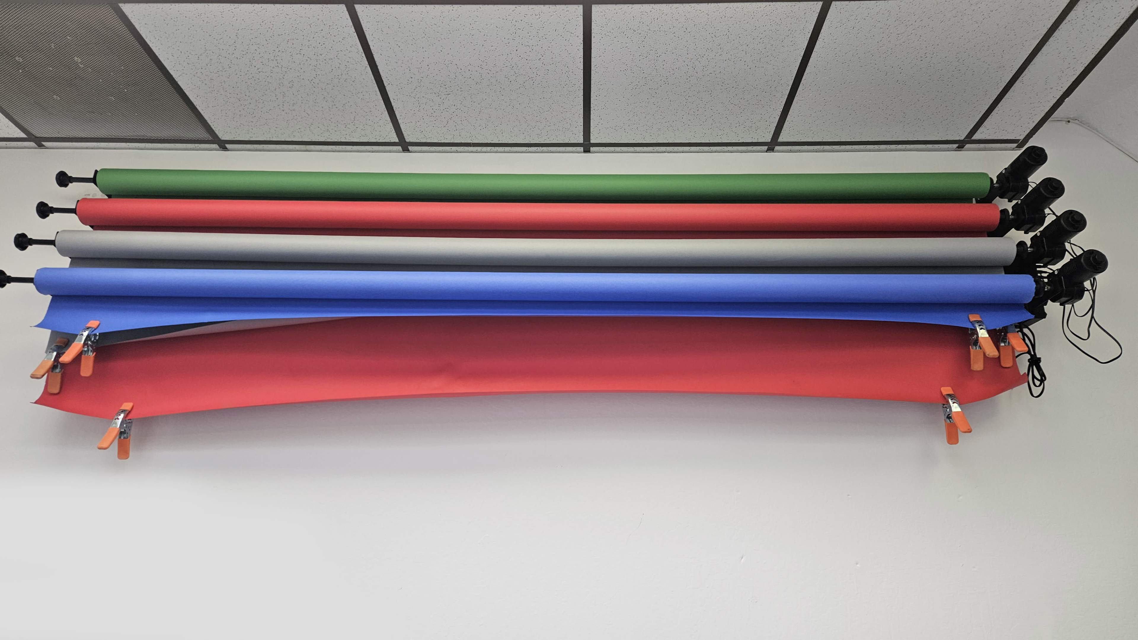 Several rolls of backdrop paper in different colors, mounted on a wall with clamps securing the ends.