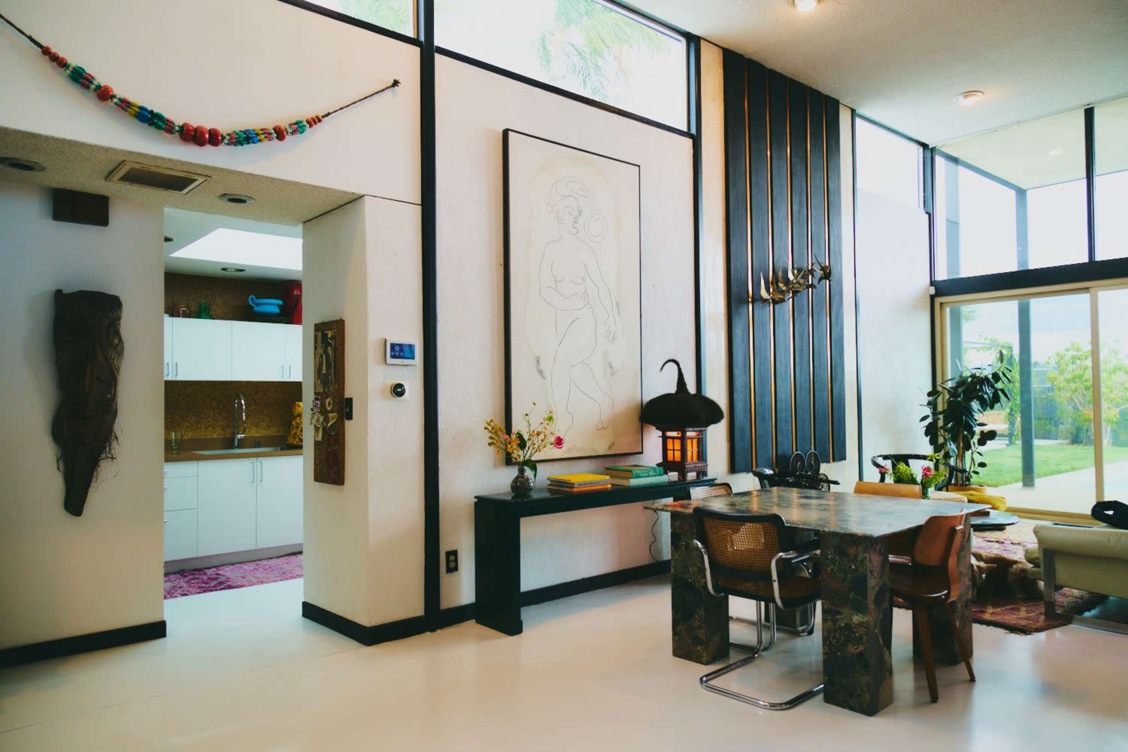 The image showcases a modern living space featuring large windows, a dining area with a textured table, and a kitchen visible in the background.