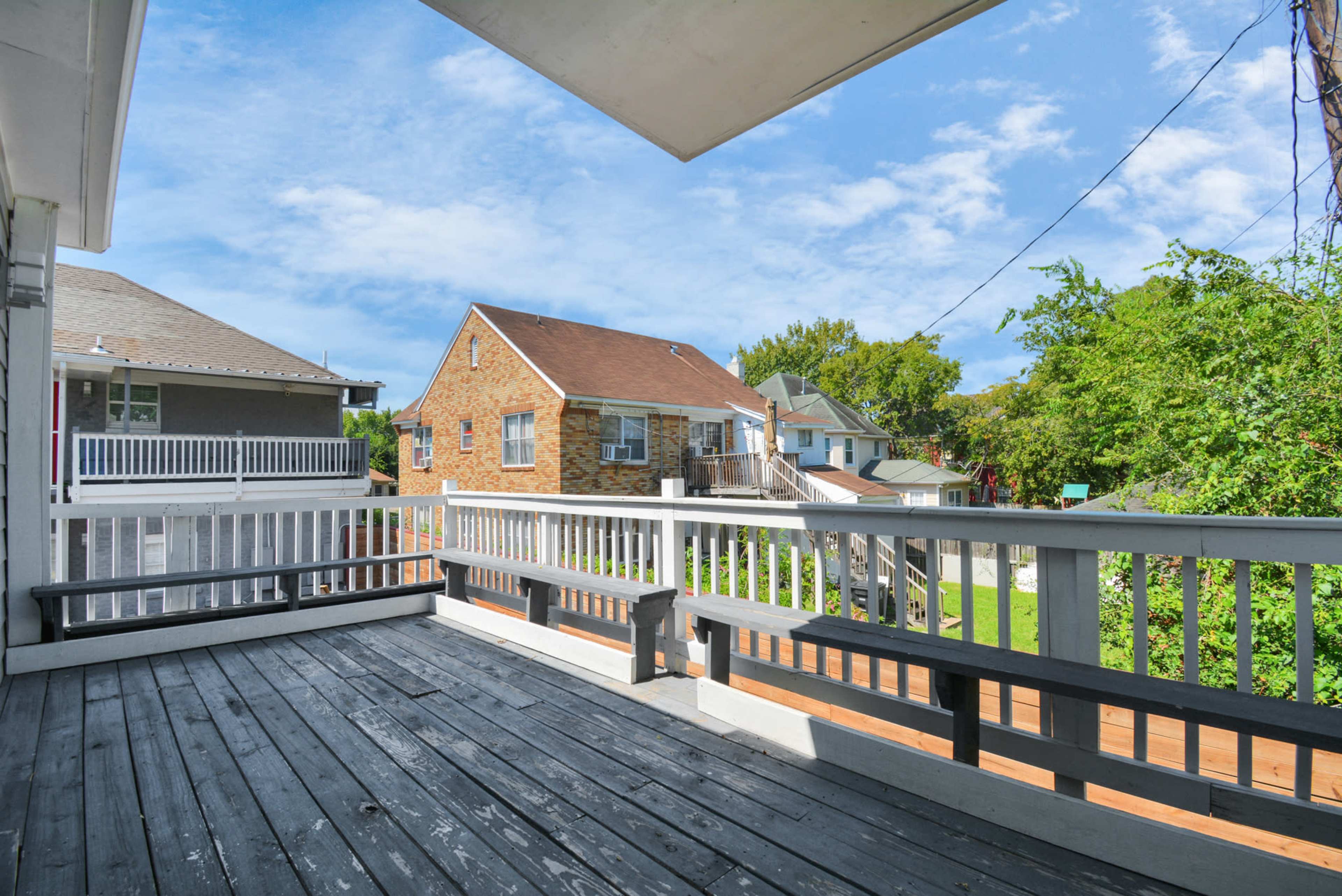 A wooden deck with benches, overlooking nearby houses and a green area under a partly cloudy sky.