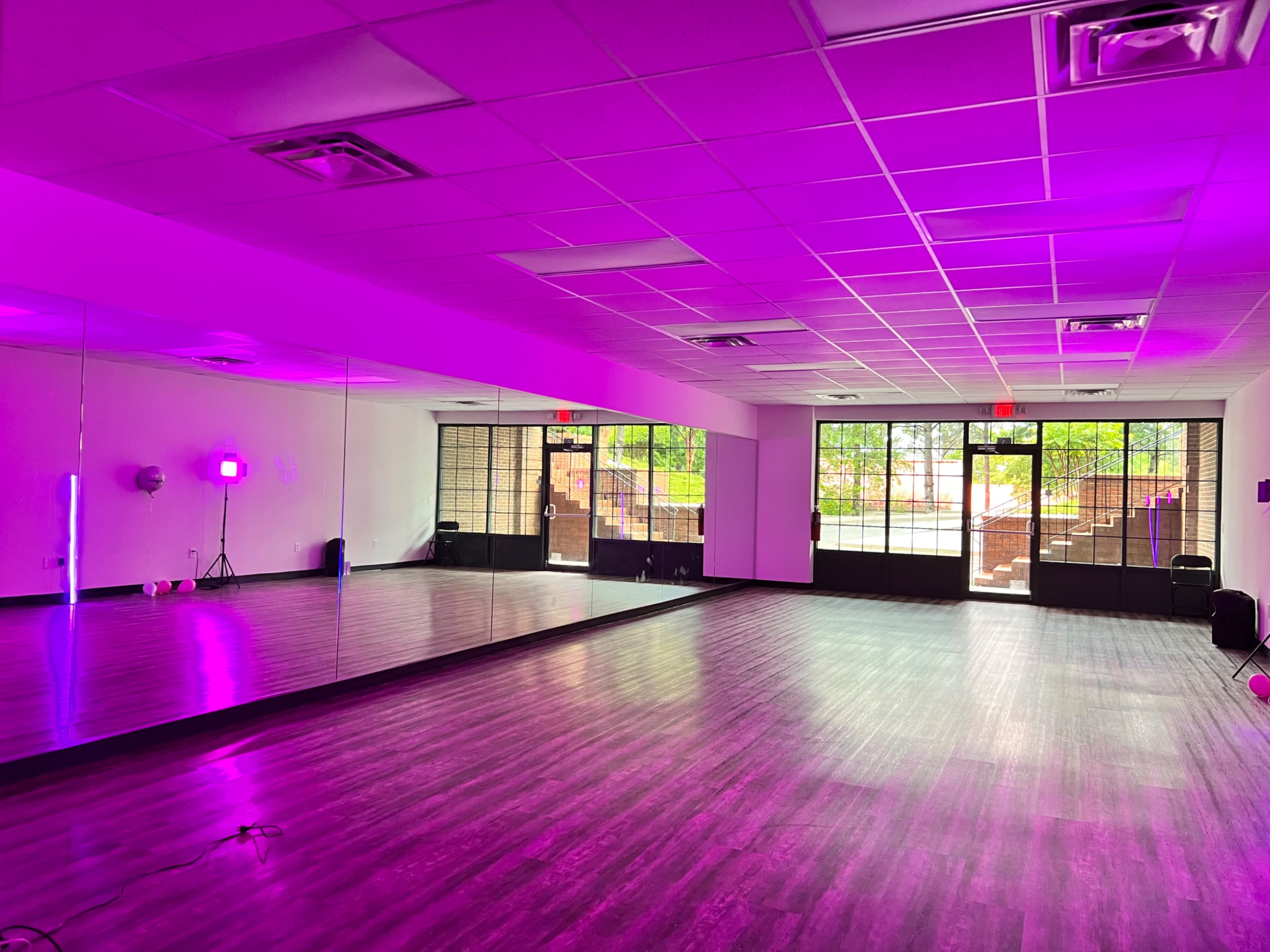 A dance studio with mirrored walls and purple lighting, featuring large windows that open to an outdoor area.