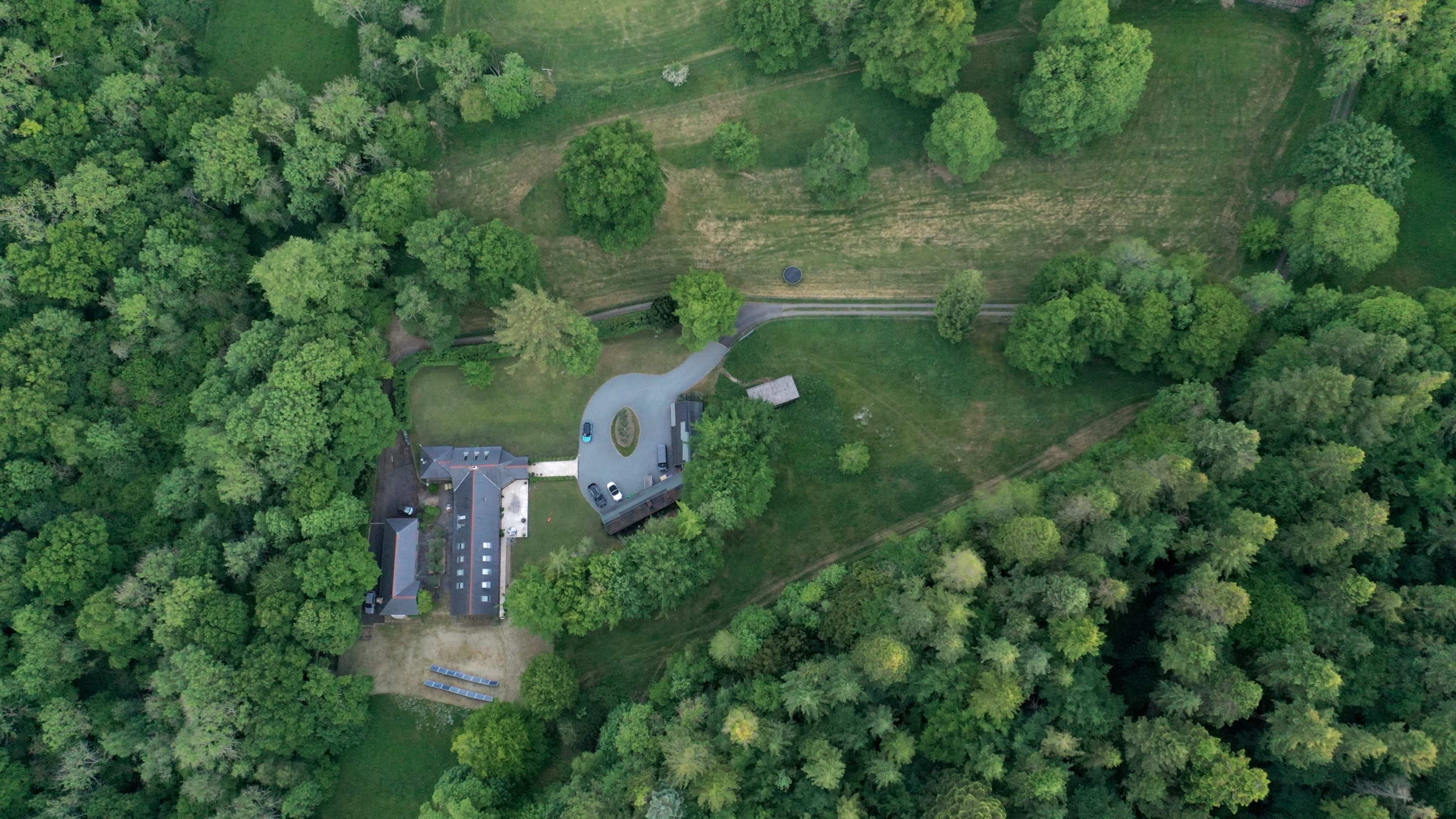 An aerial view shows a large house surrounded by dense greenery and open grassy areas.