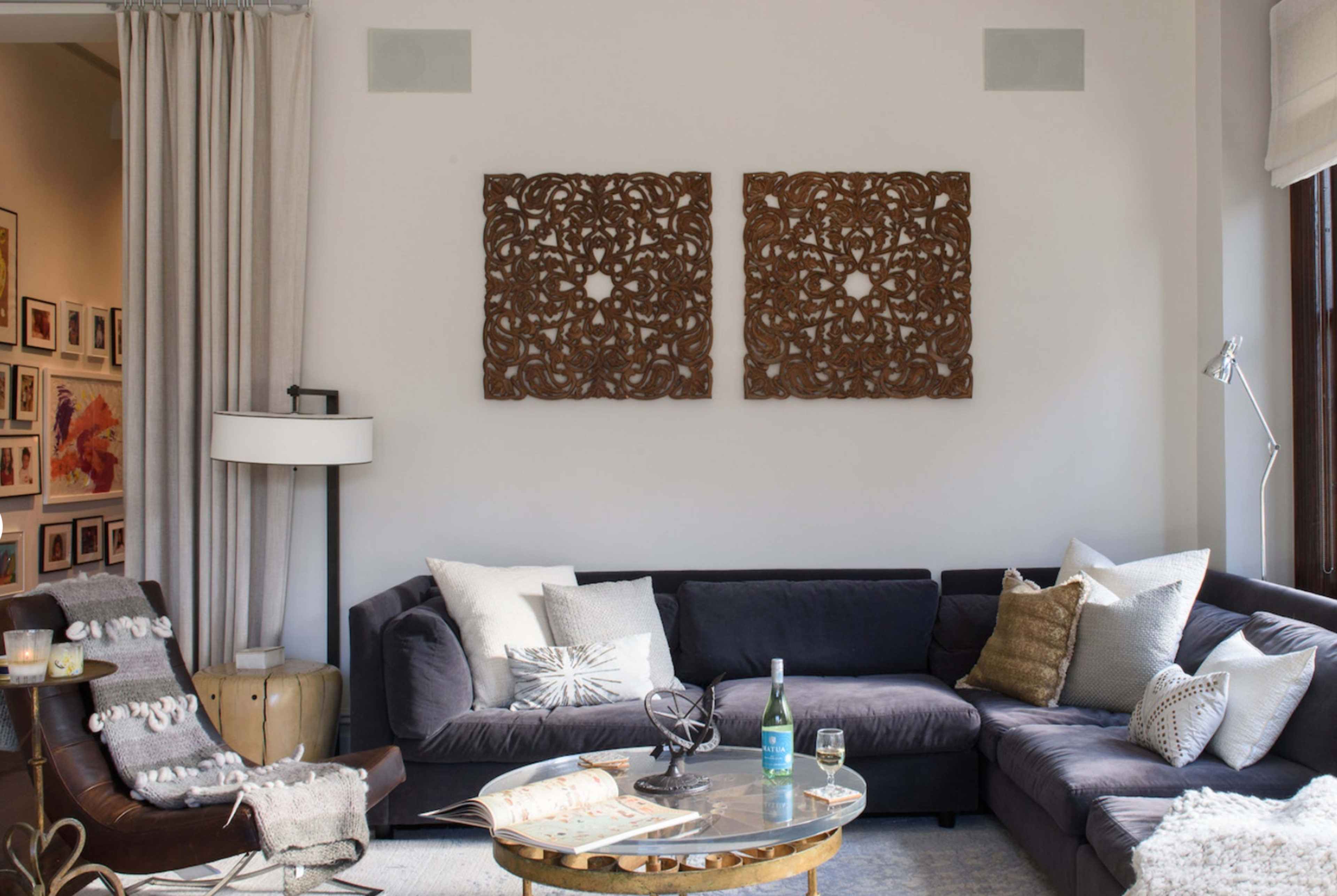 A stylish living room featuring a dark sectional sofa, decorative wall art, a round coffee table with a glass of wine, and a floor lamp.
