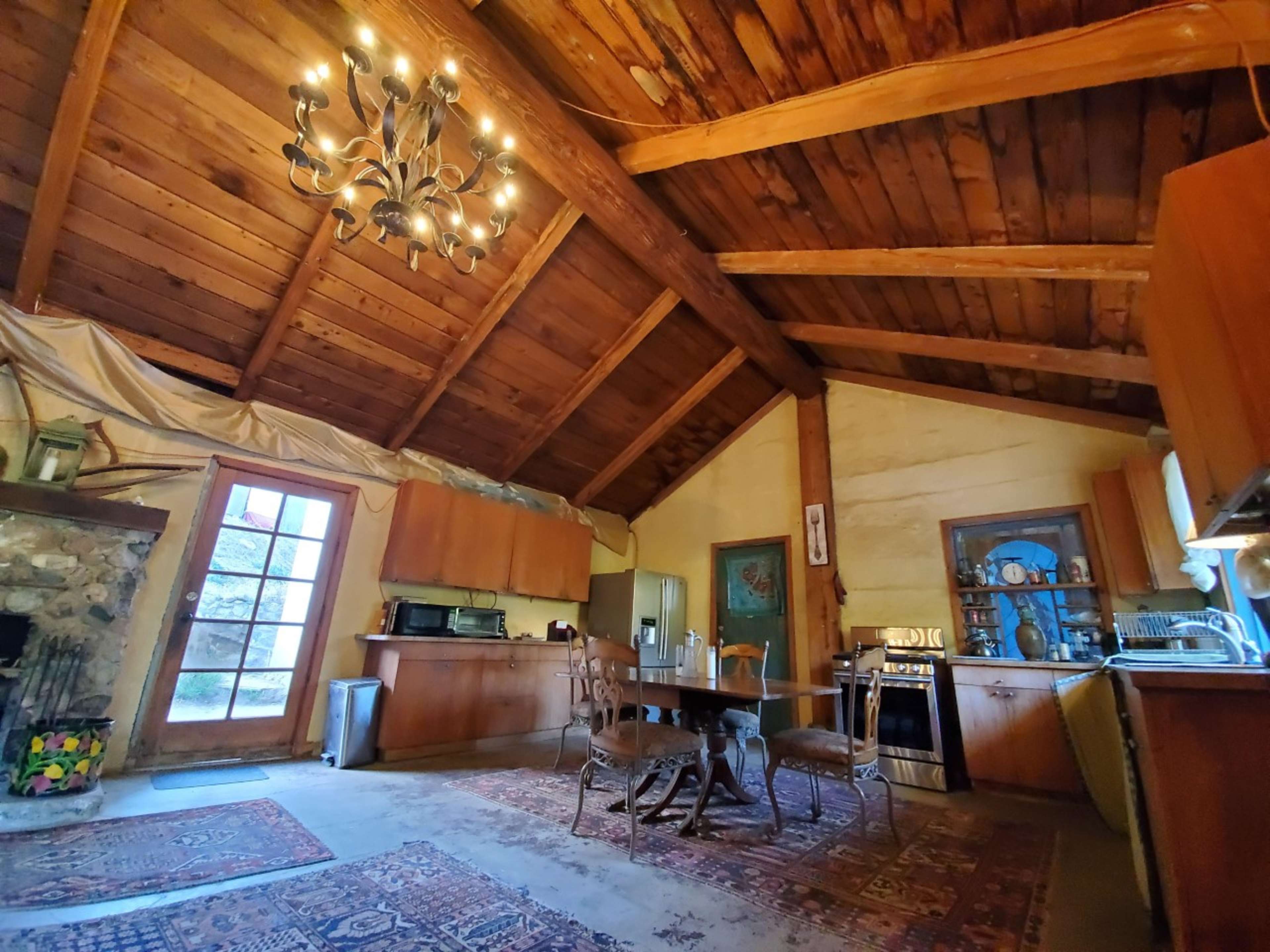A rustic kitchen with wooden ceilings, stone walls, and a dining table surrounded by chairs.
