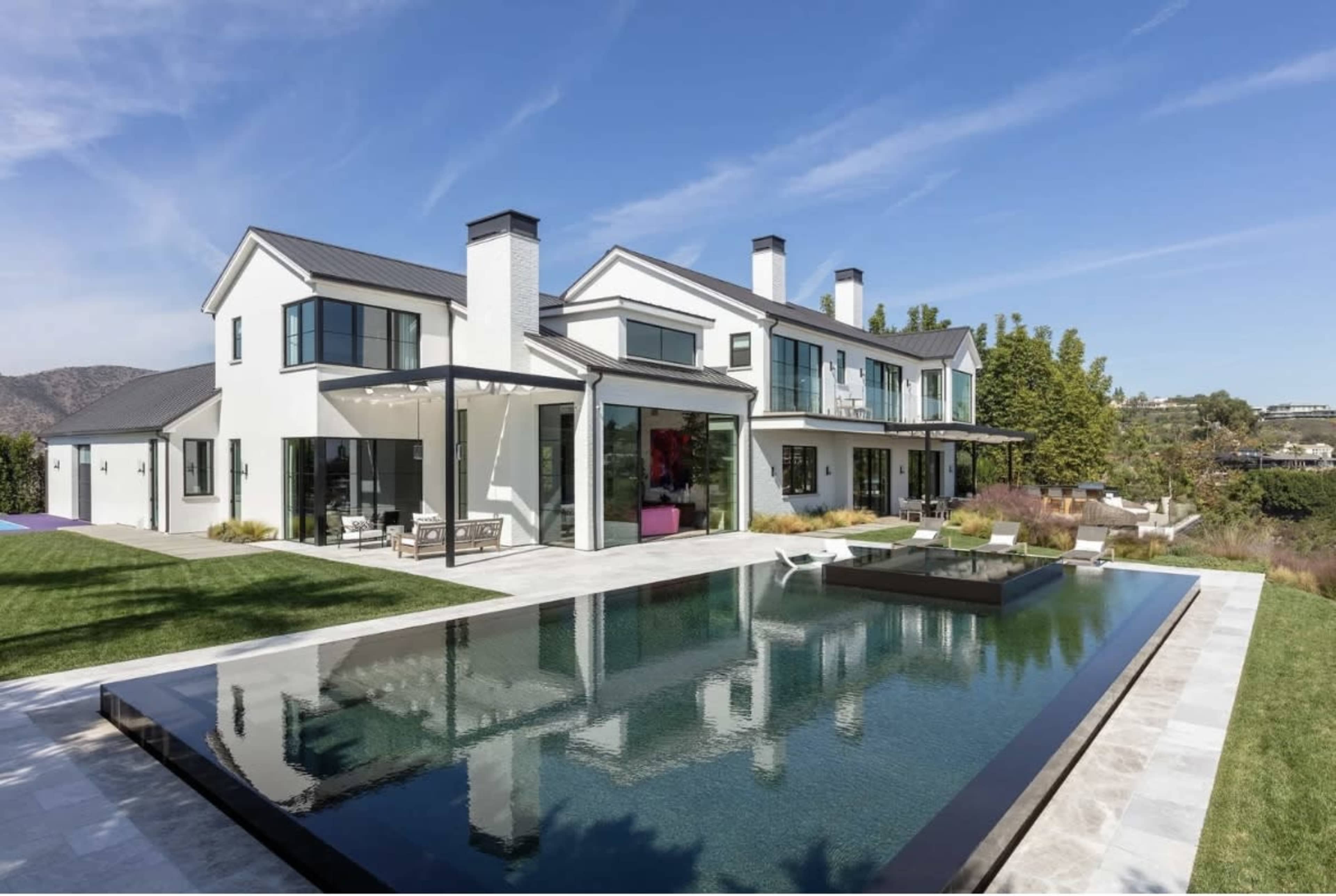 The image features a modern two-story white house with large windows, surrounded by a well-manicured lawn and a reflective swimming pool.