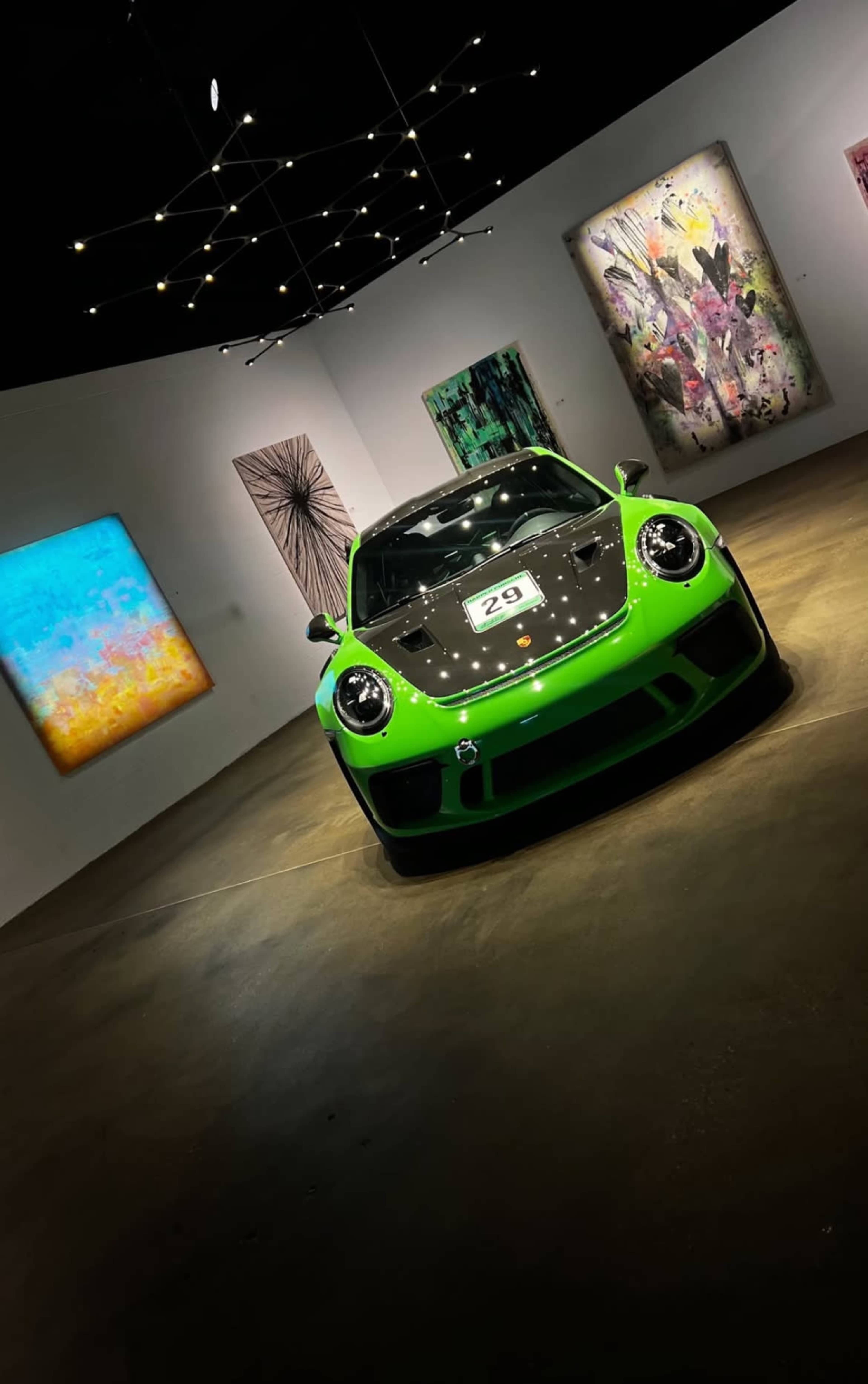 A bright green sports car is positioned in a modern art gallery, surrounded by colorful abstract paintings.