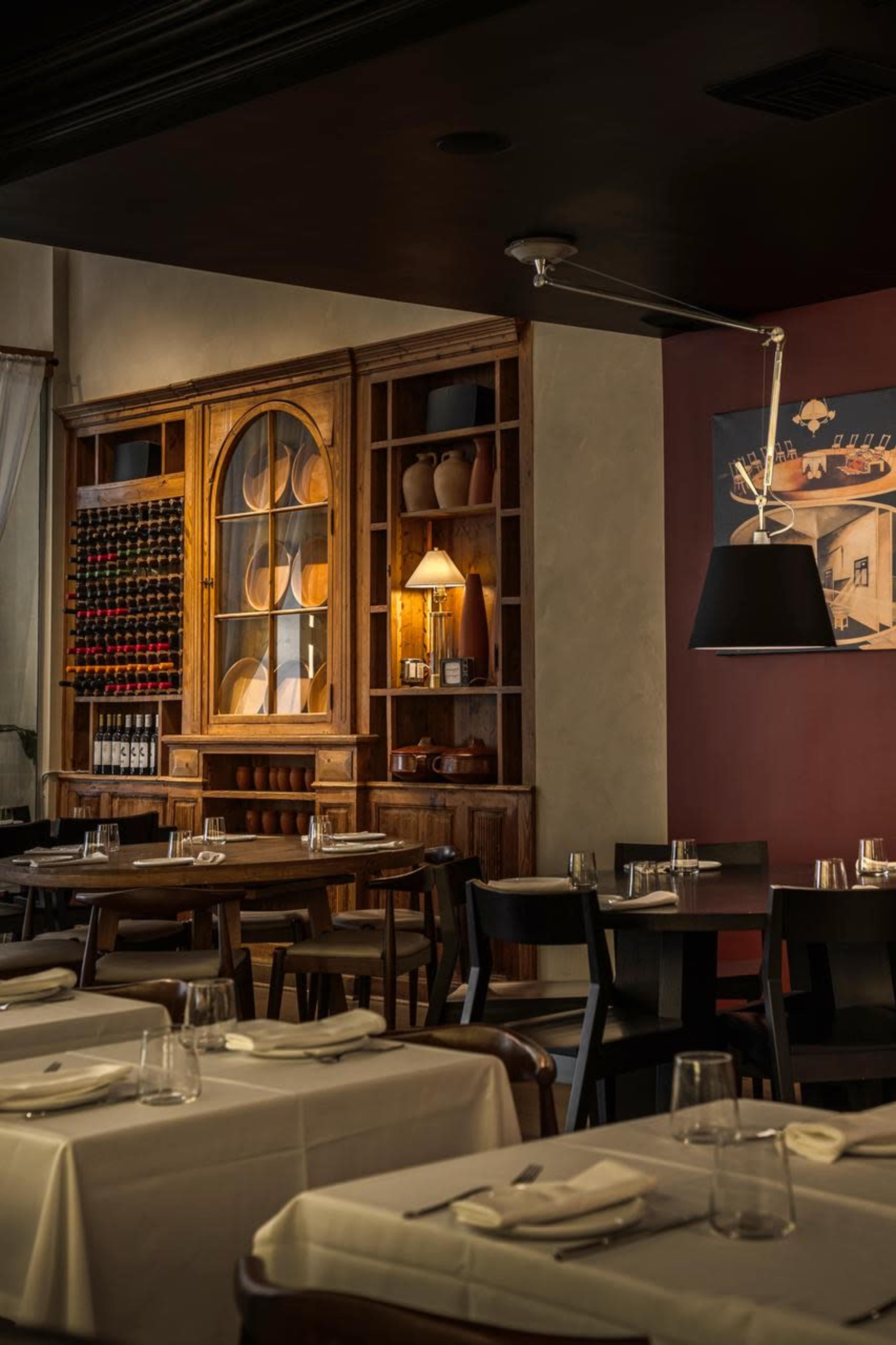 The image shows a restaurant interior featuring wooden shelving with decorative items, a wine rack, and neatly arranged tables with white tablecloths.