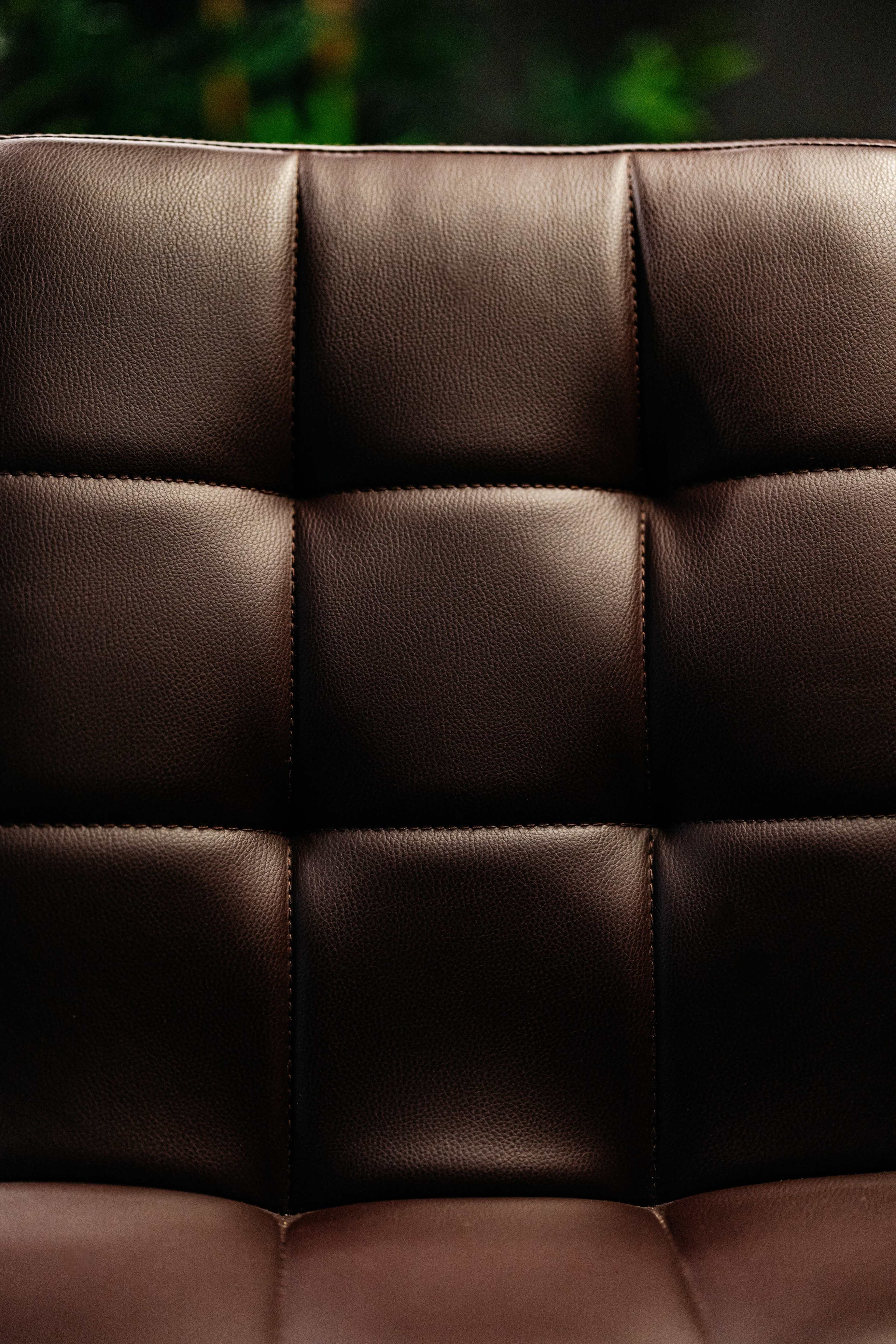 A close-up of a brown leather chair with a quilted pattern on its backrest.