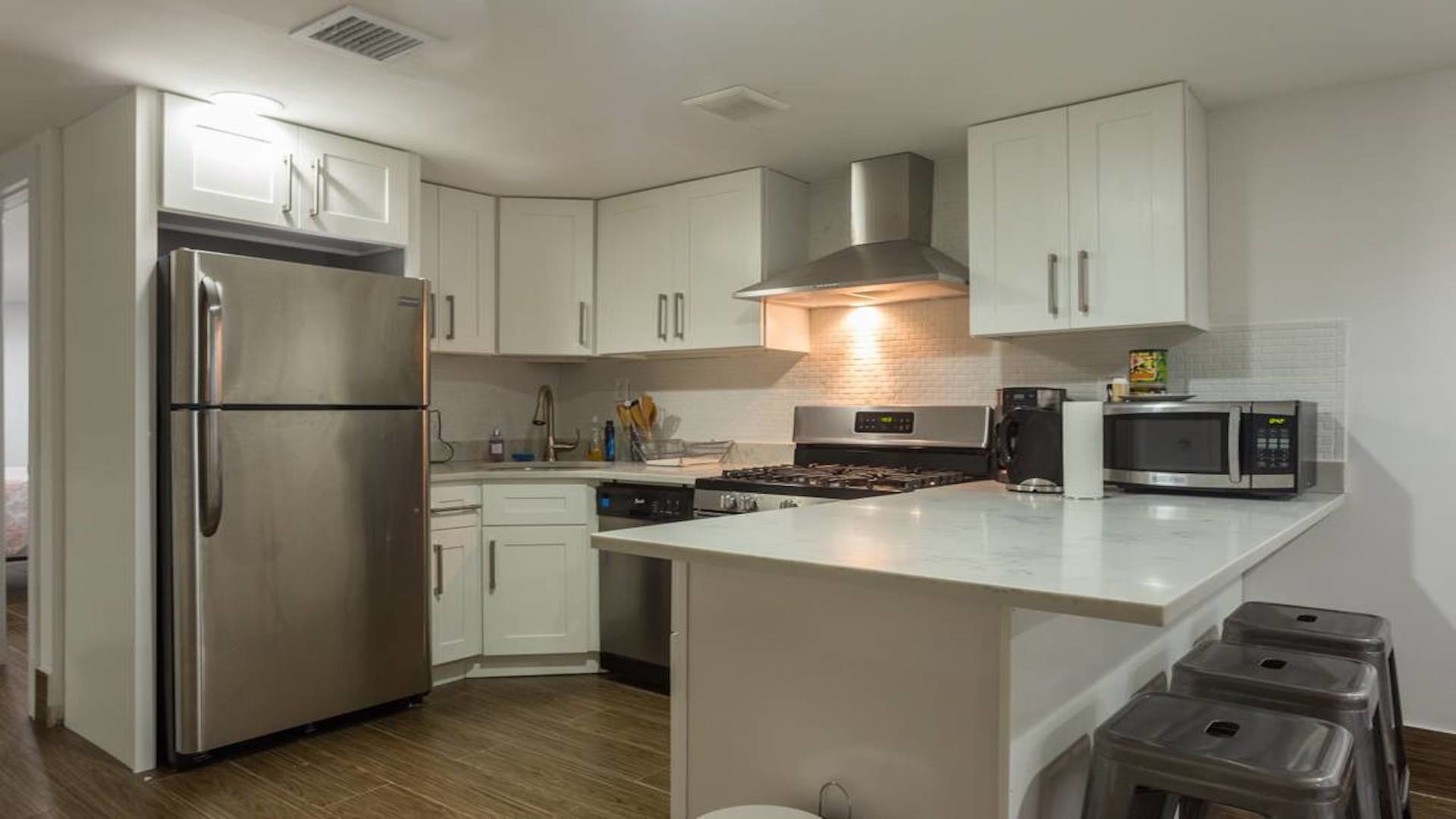 A modern kitchen features stainless steel appliances, white cabinetry, and a marble countertop with bar seating.