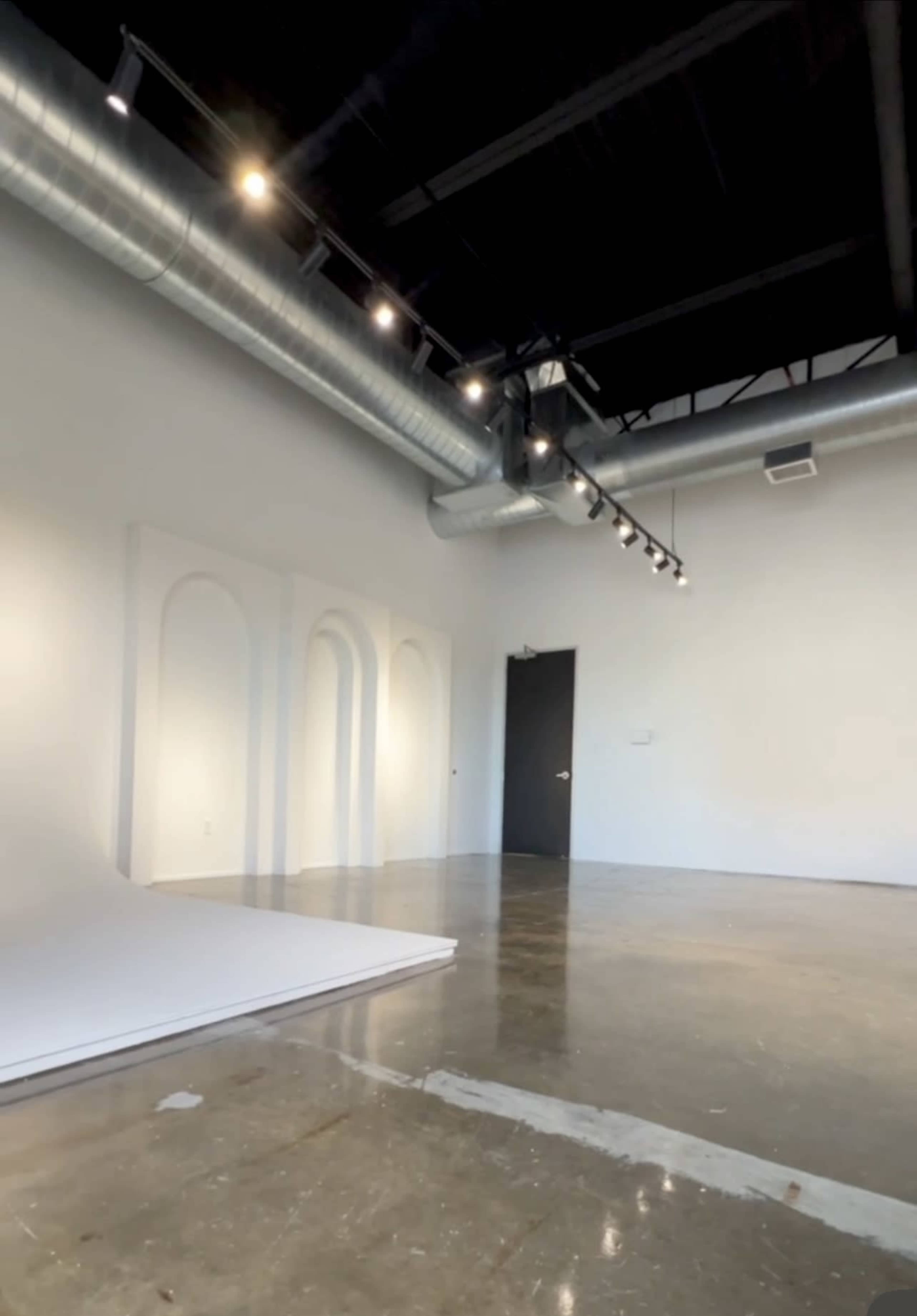 An empty gallery space with a polished concrete floor, curved wall features, and track lighting.