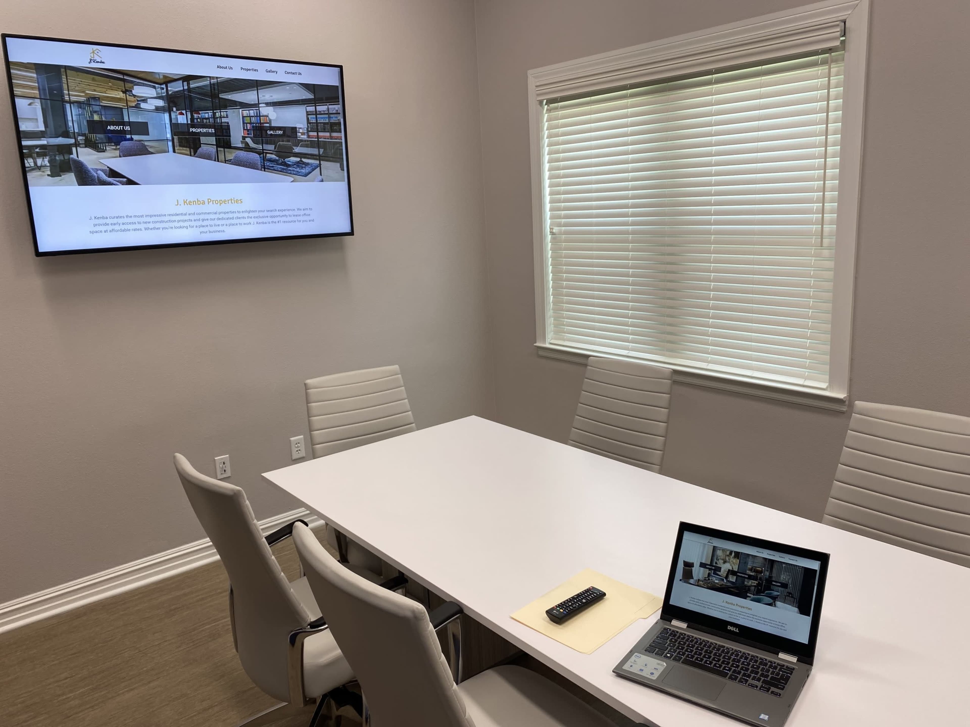 A conference room is shown with a large screen displaying a webpage and a laptop open on a table.