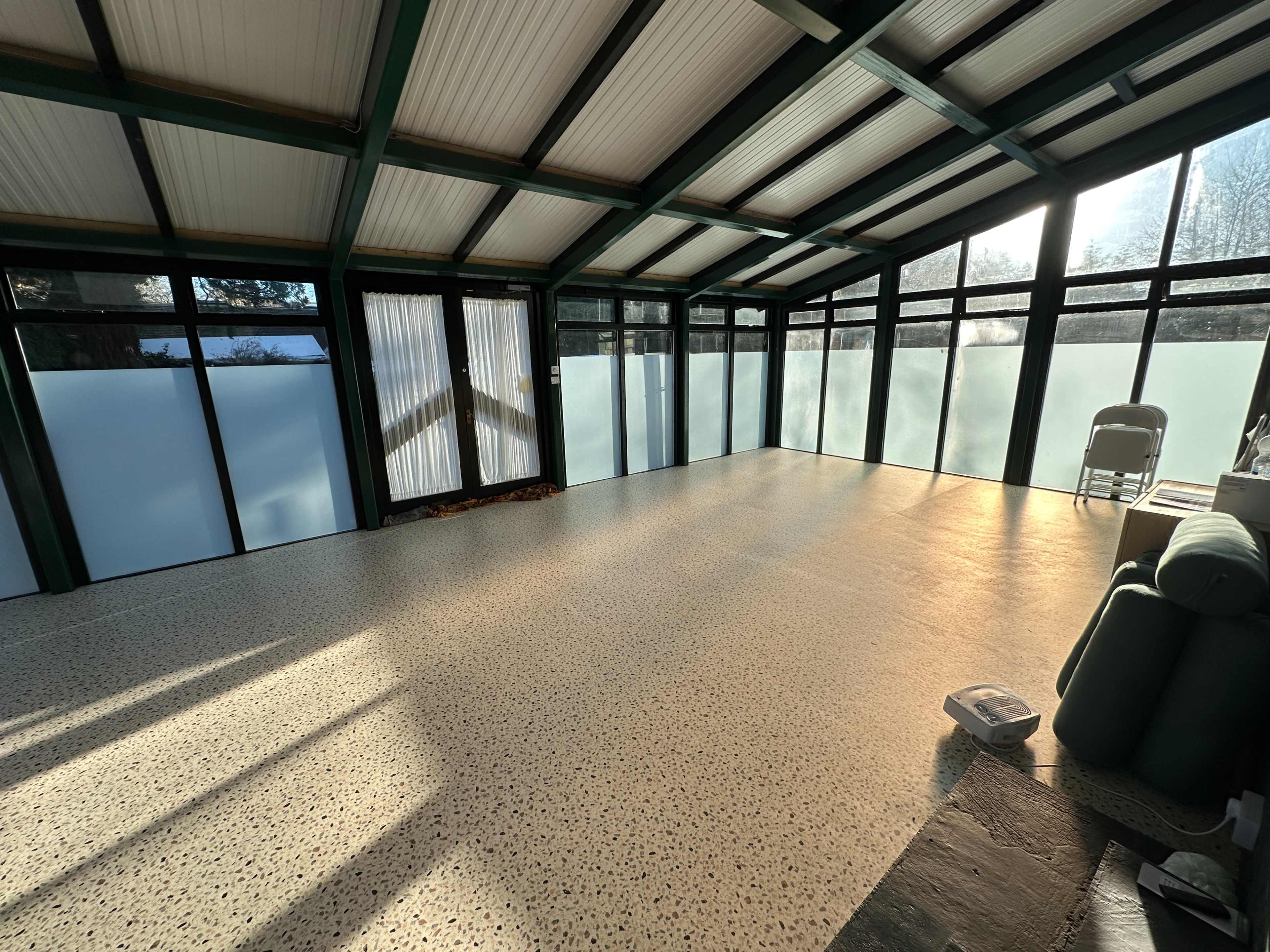 The image shows a spacious sunroom with large glass panels, a smooth floor, and natural light streaming in.