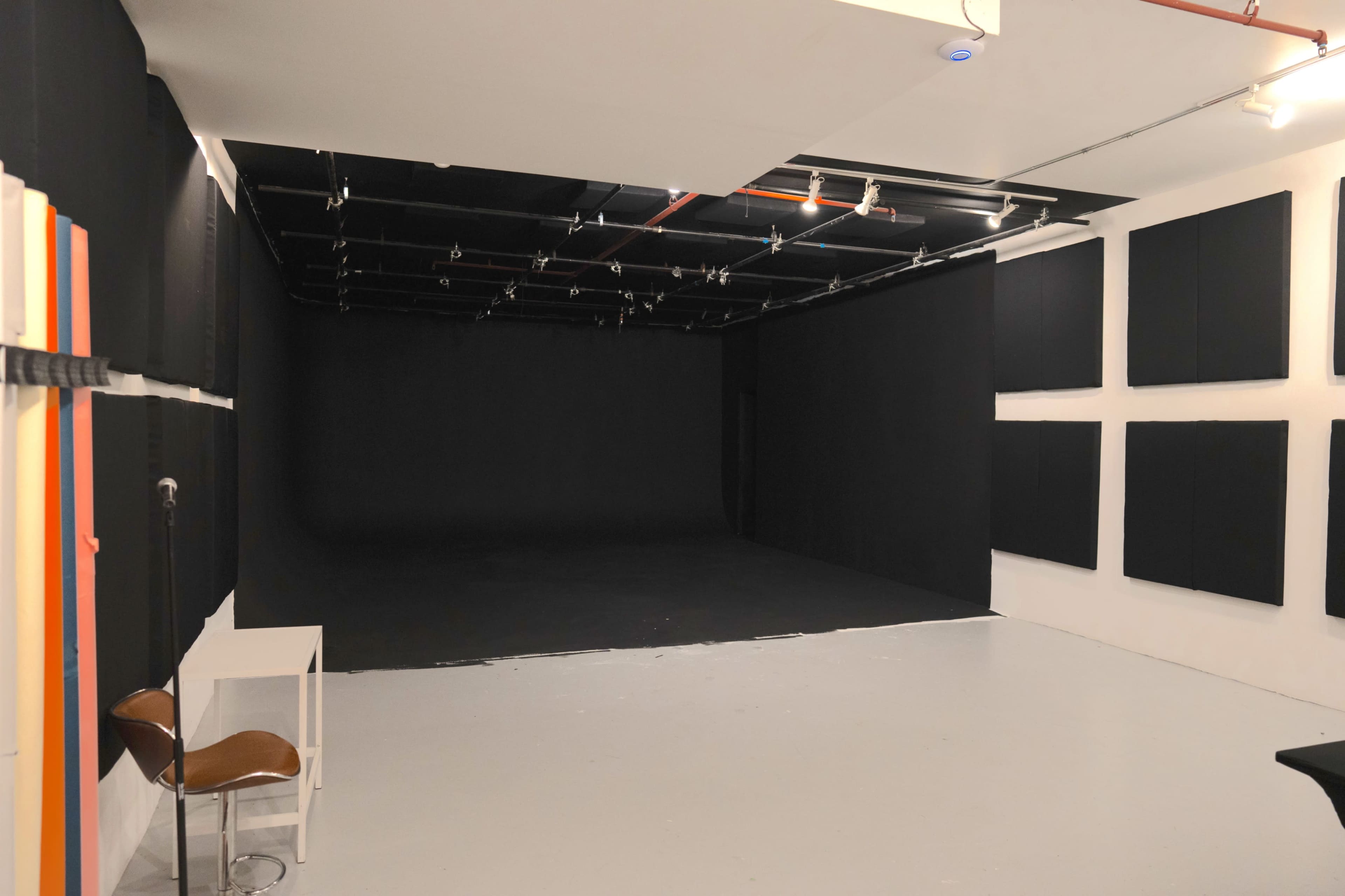 The image shows a spacious studio with black walls and soundproof panels, featuring a plain white floor and minimal furniture.