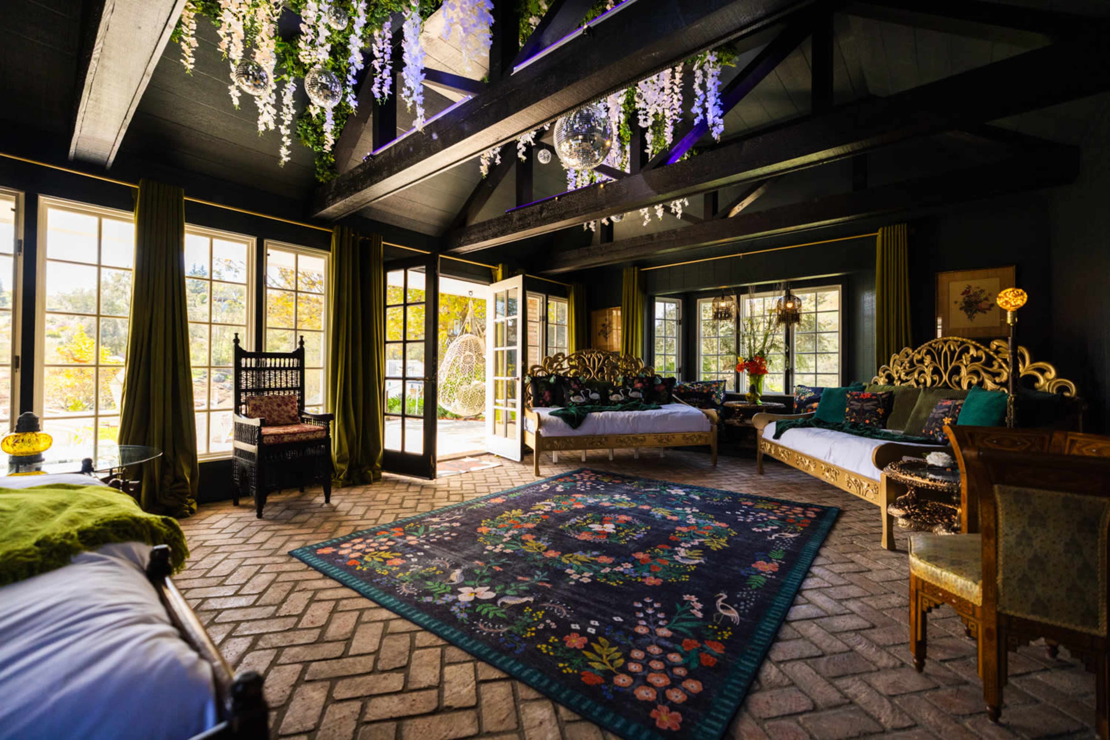 The room features a spacious layout with multiple seating areas, large windows allowing natural light, and decorative plants hanging from the ceiling.