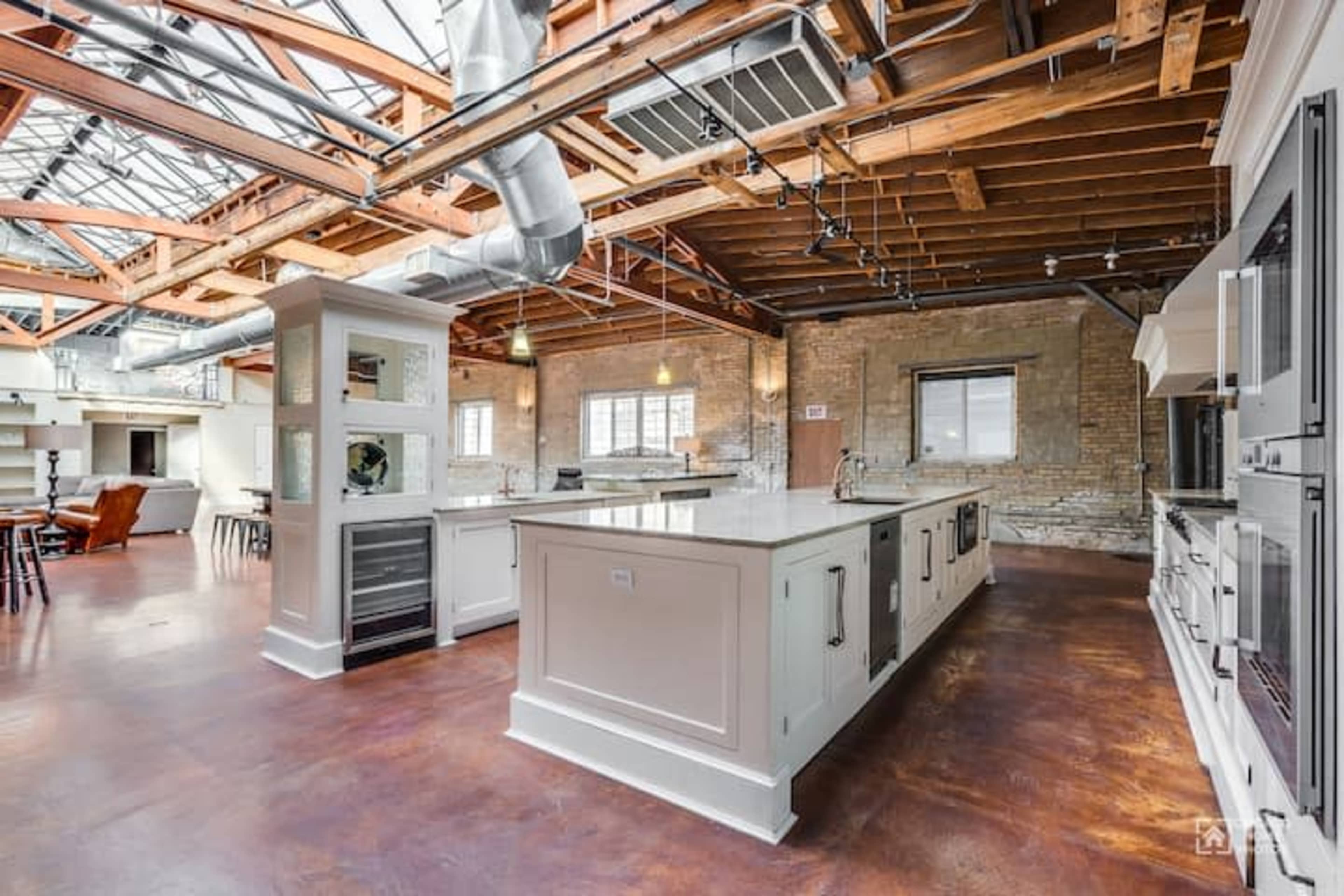A spacious kitchen with a central island, high ceilings, exposed wooden beams, and large windows allowing natural light.