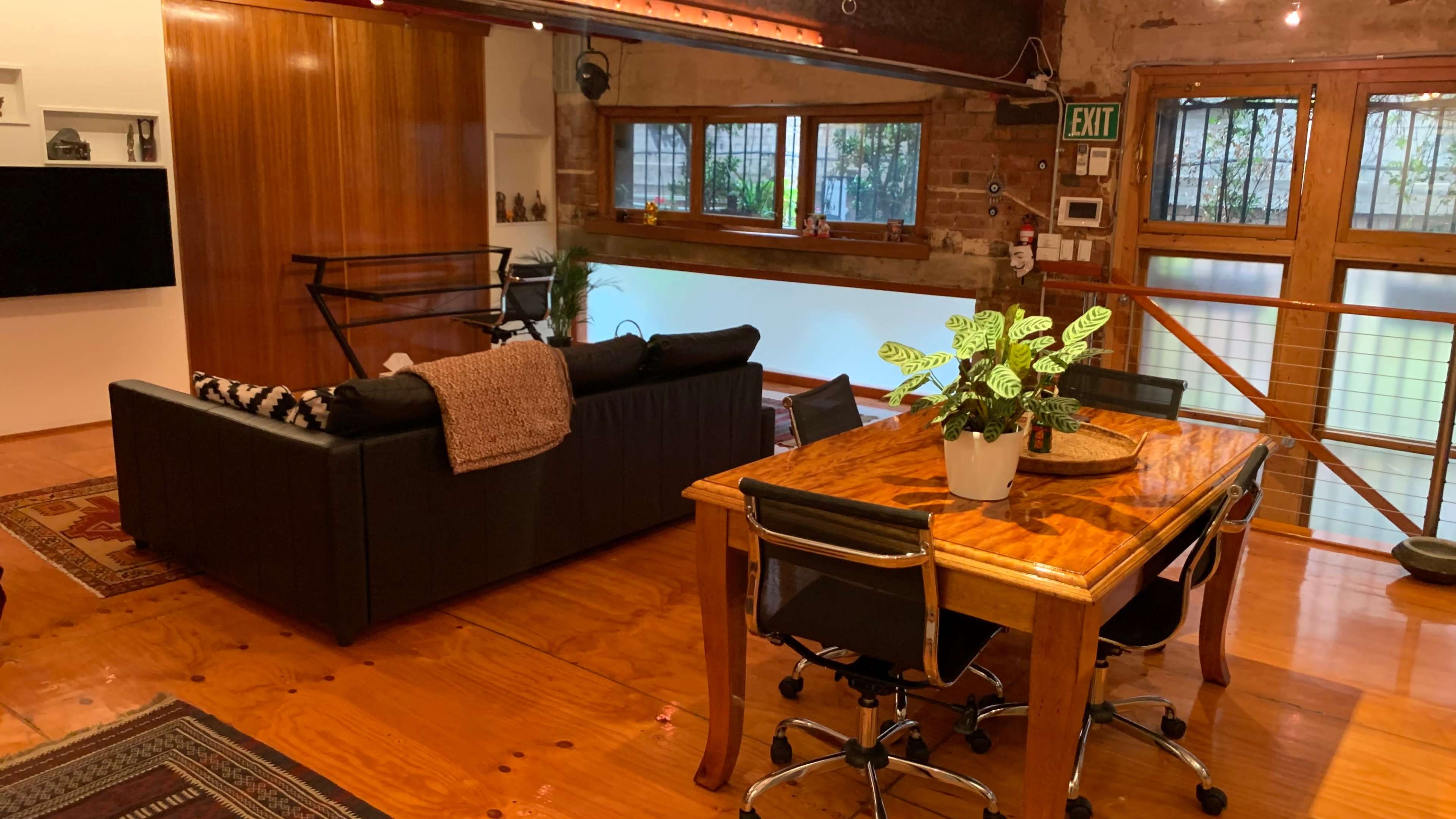 A spacious living area with a black sofa, a wooden dining table with chairs, and large windows allowing natural light.