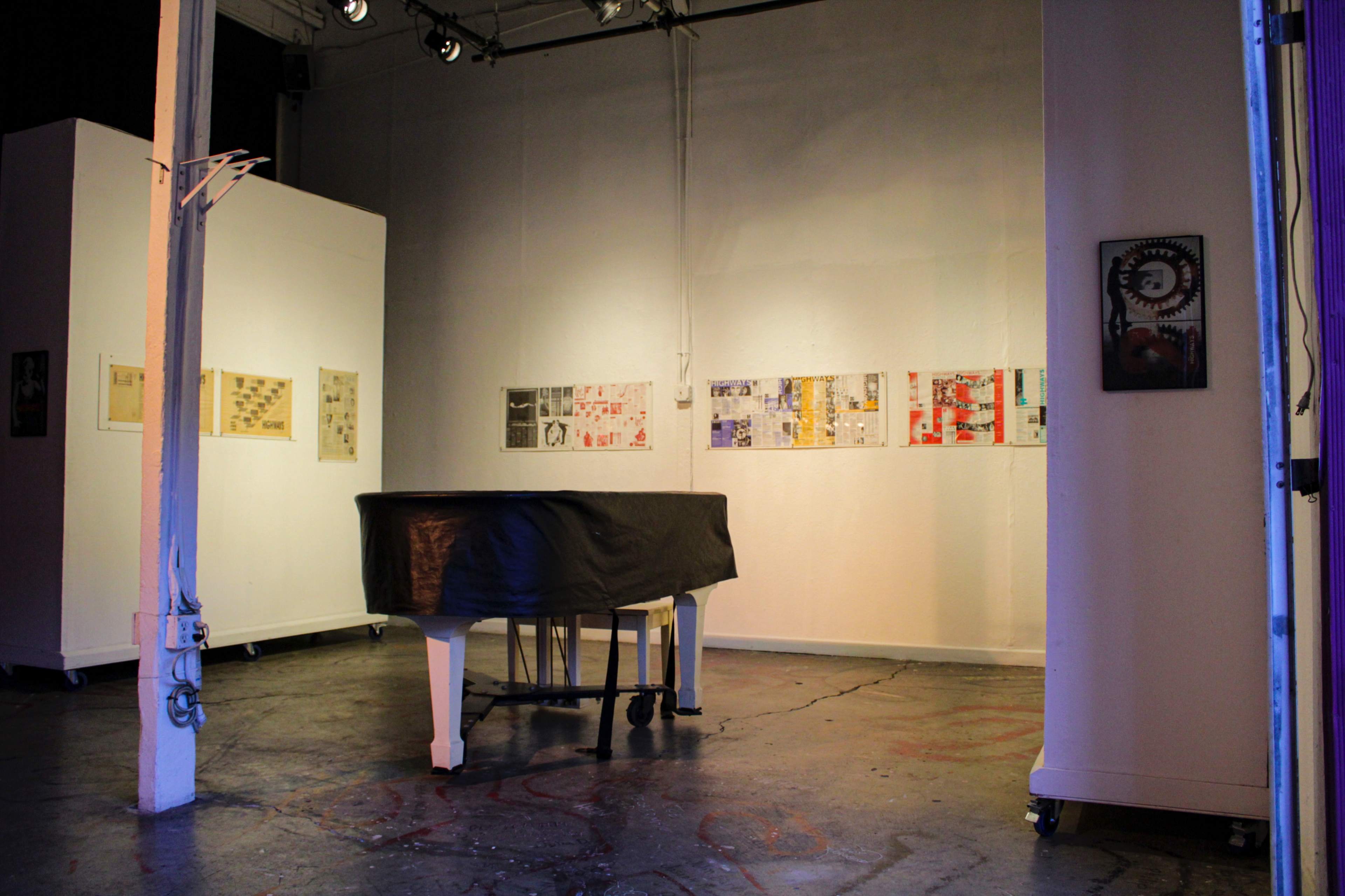 An art gallery with a covered piano in the foreground and framed artworks displayed on the walls.