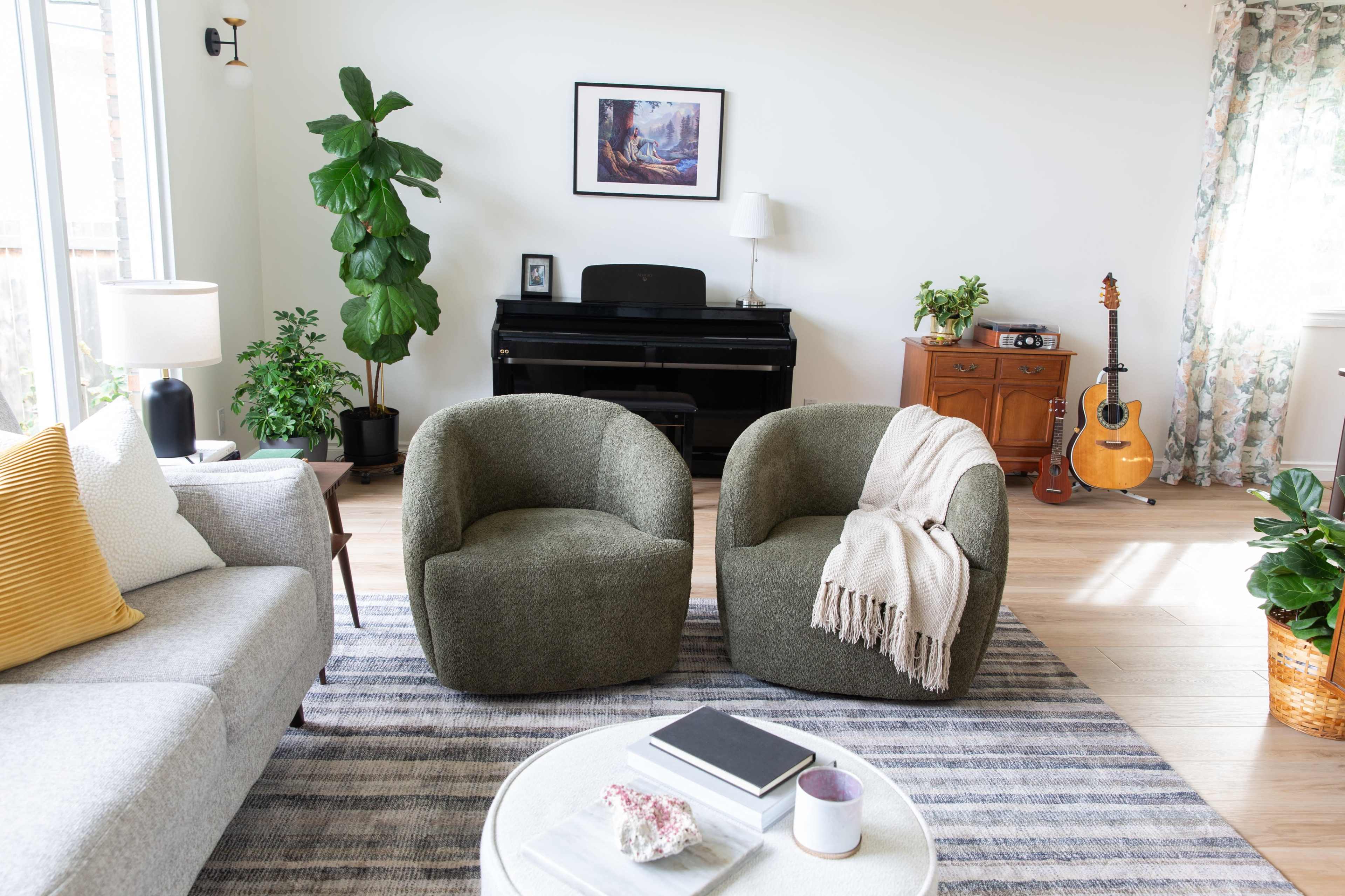 The living room features two round armchairs facing each other, a gray sofa, a small coffee table, and a piano in the background, with plants and a guitar adding decorative elements.