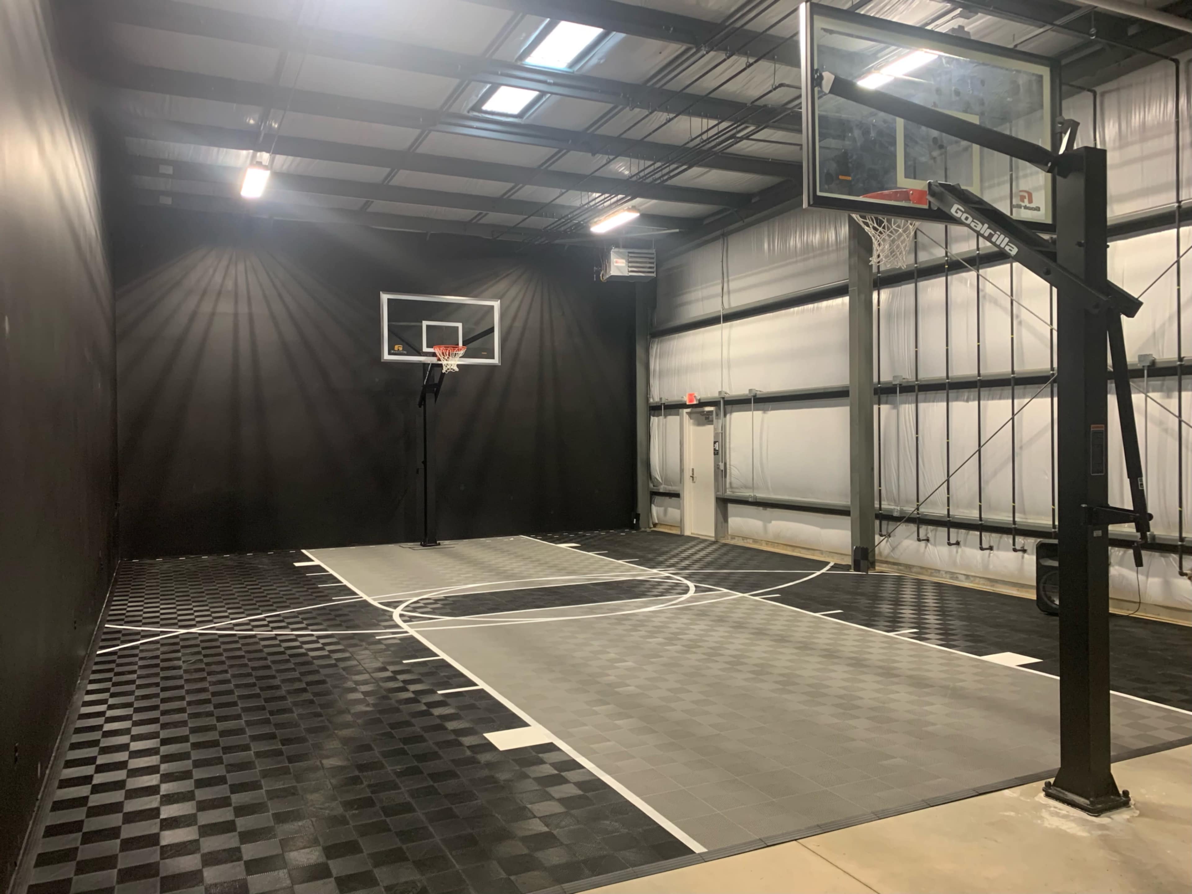 An indoor basketball court with a black background, featuring a basketball hoop and a checkered floor design.
