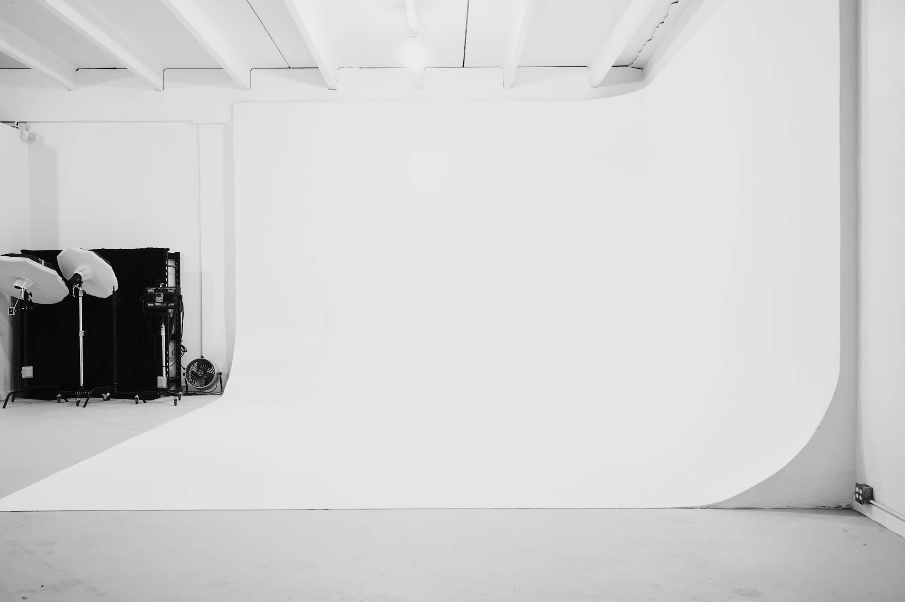A photography studio with a large, white seamless backdrop and studio lighting equipment arranged to the side.