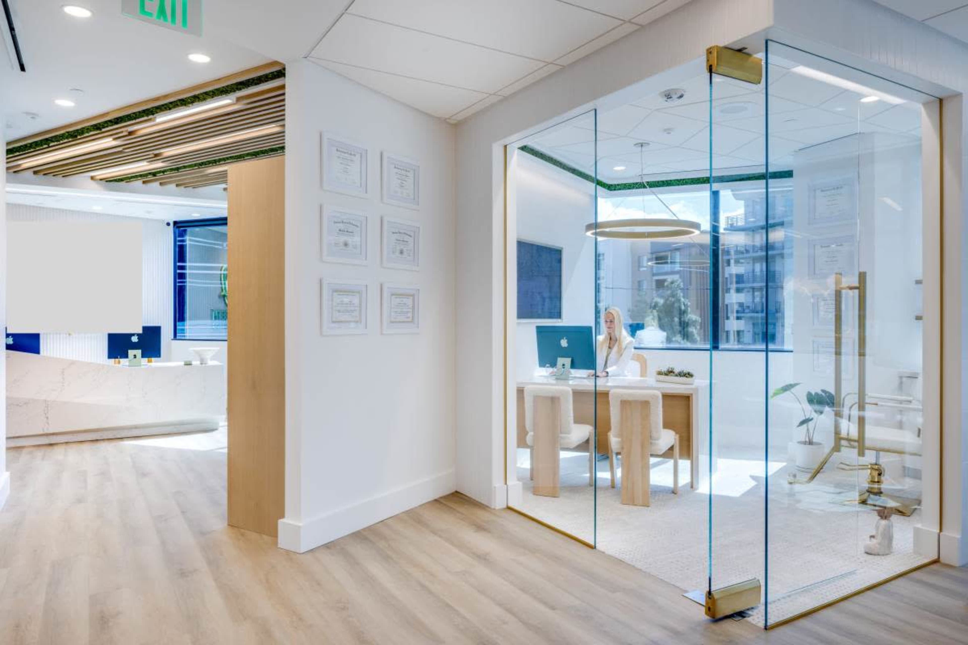 The image shows a modern office interior with a glass meeting room and a woman working at a desk.