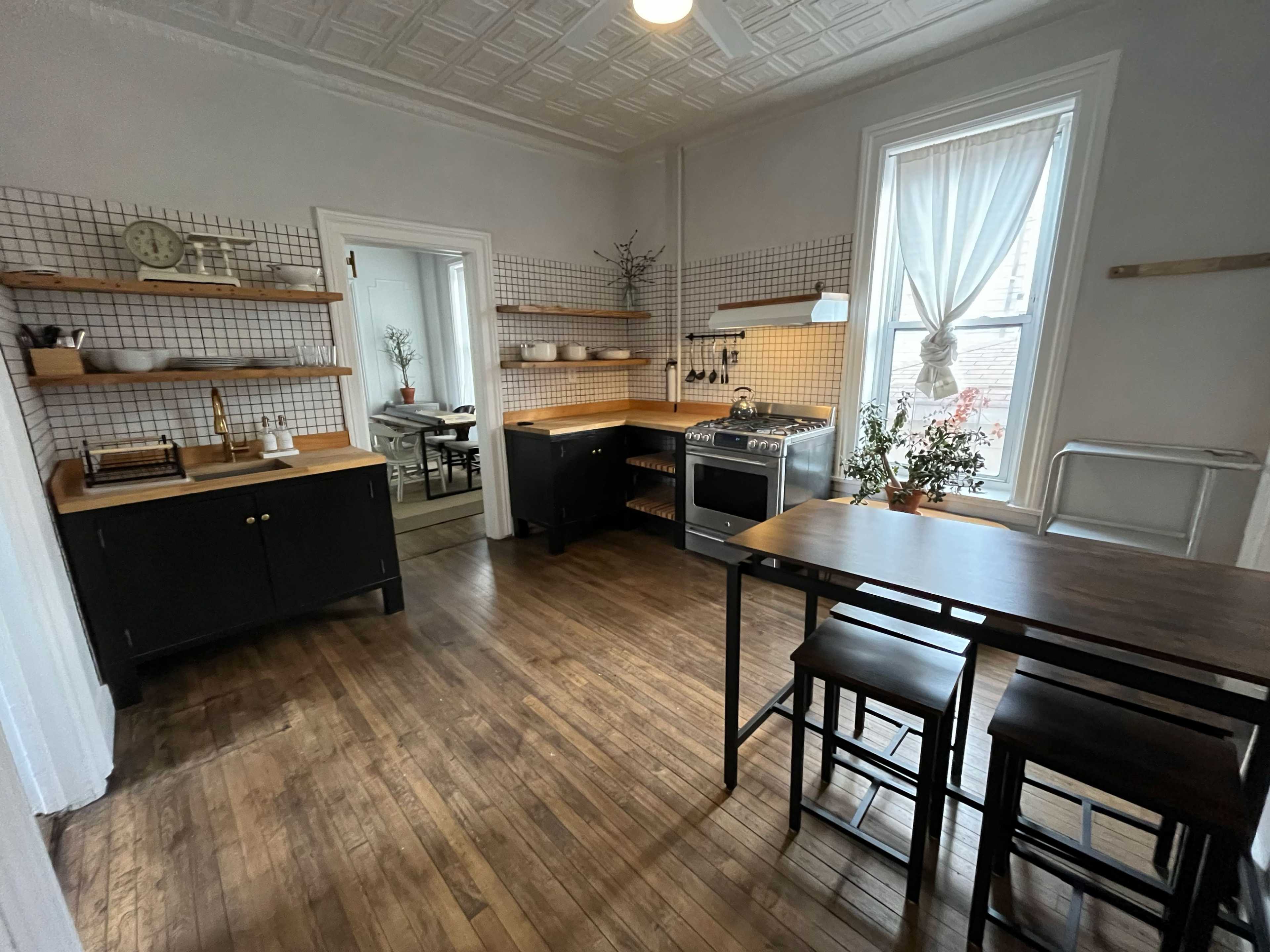 A spacious kitchen with black cabinetry, wooden countertops, open shelving, and a dining table with chairs.