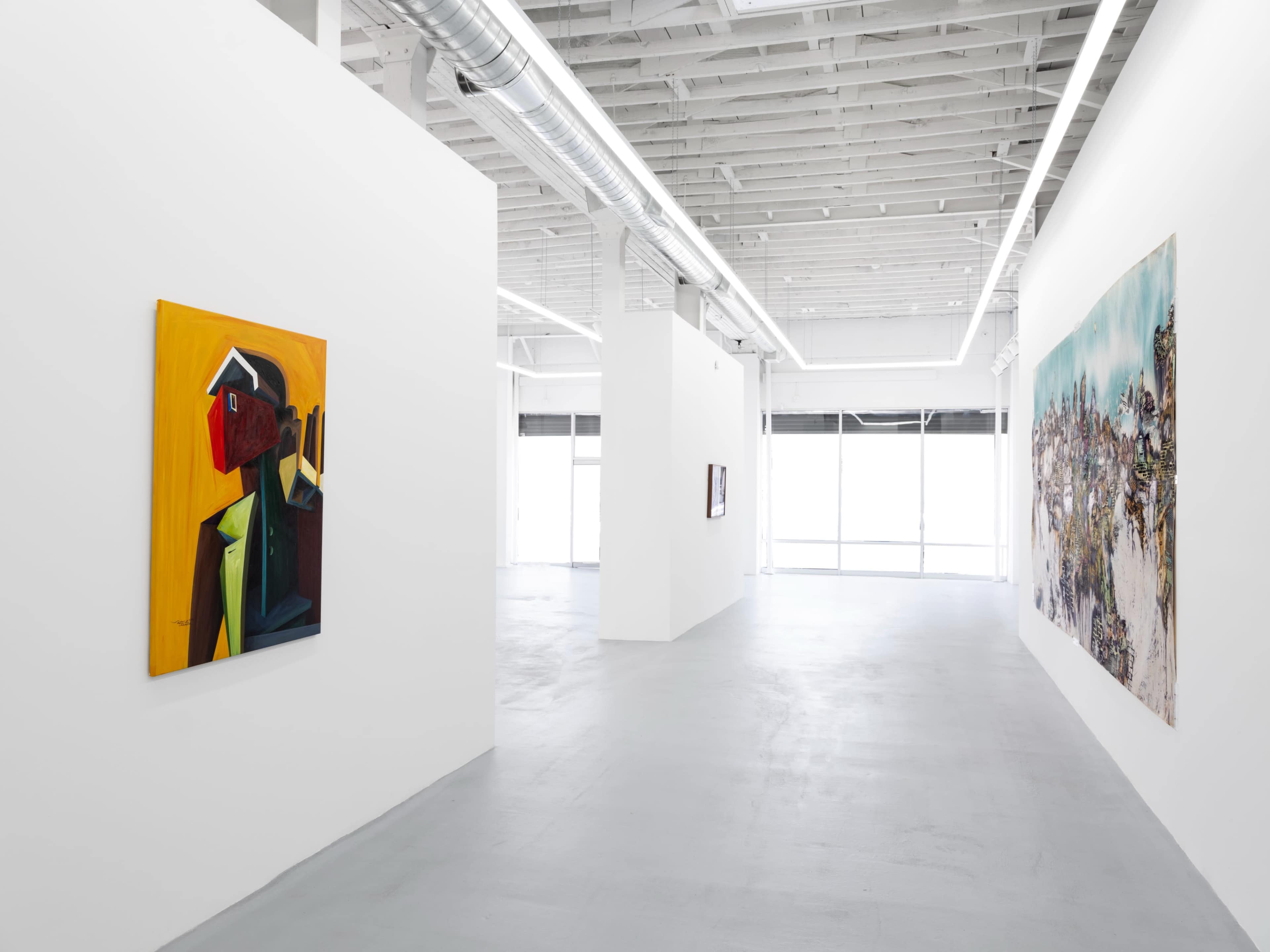 A spacious art gallery featuring two large paintings on the walls and ample natural light filtering through large windows.