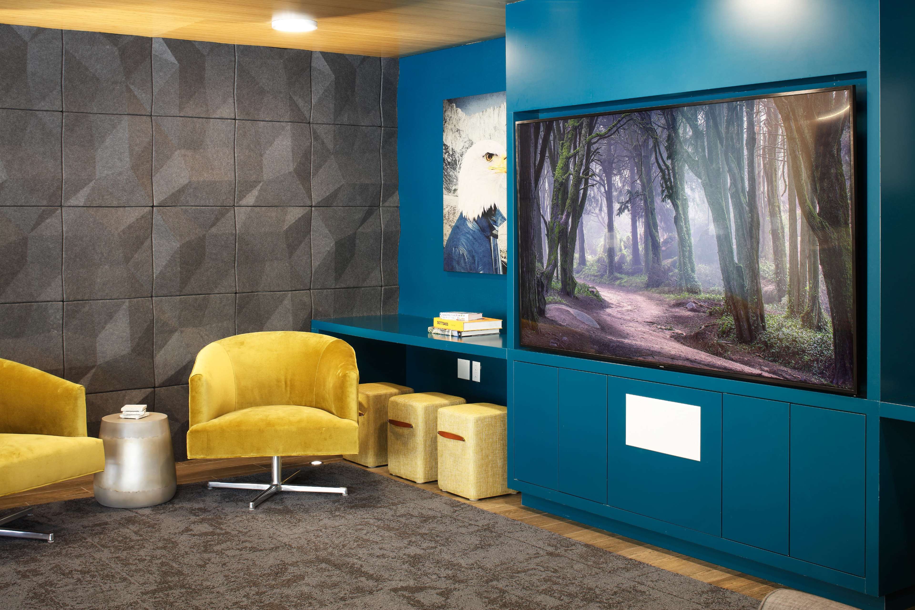 A modern living space featuring two yellow chairs, a large television displaying a forest scene, and a textured gray wall.