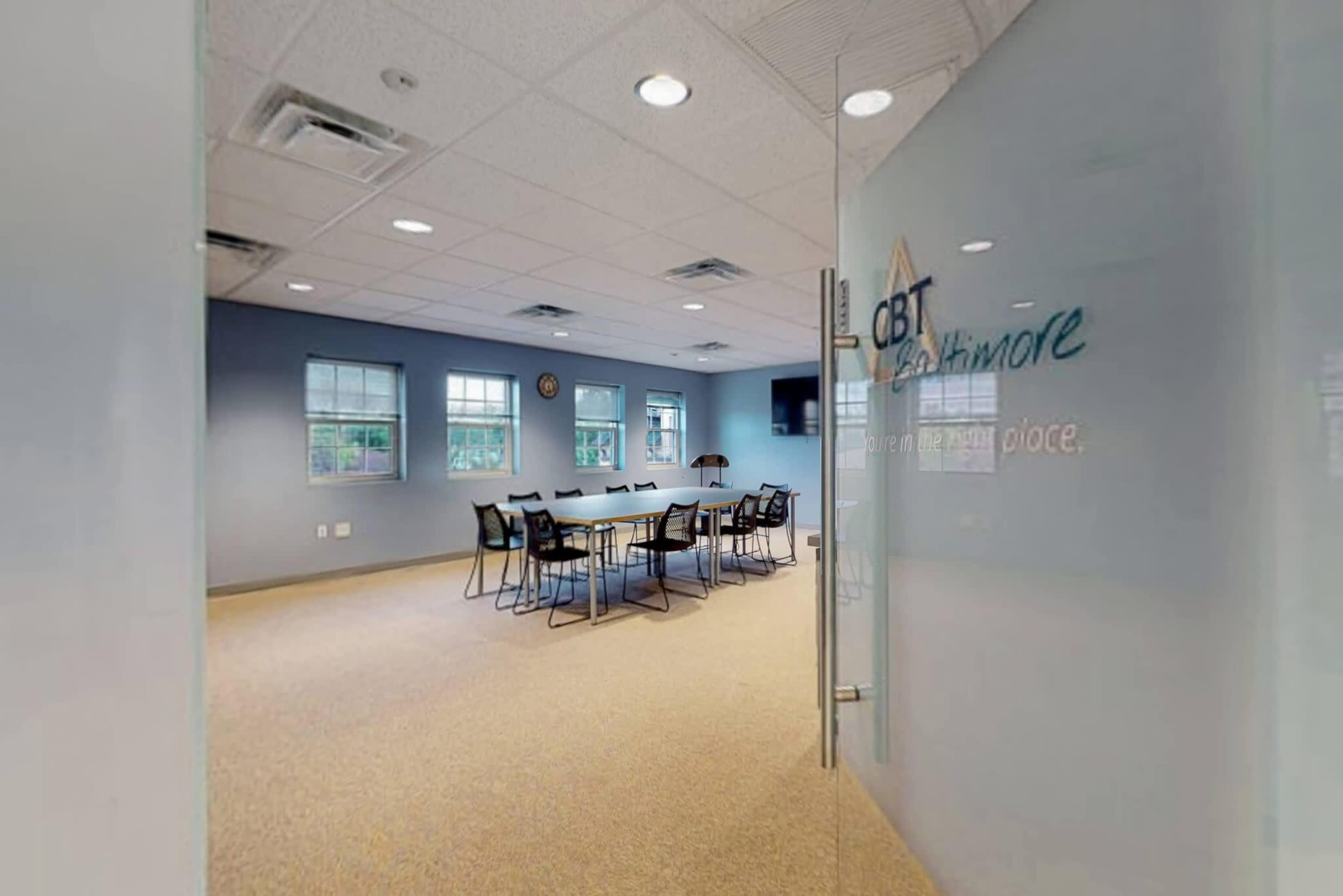 A conference room with a long table and chairs, featuring blue walls and windows, is visible through a glass door labeled "CBT Baltimore."