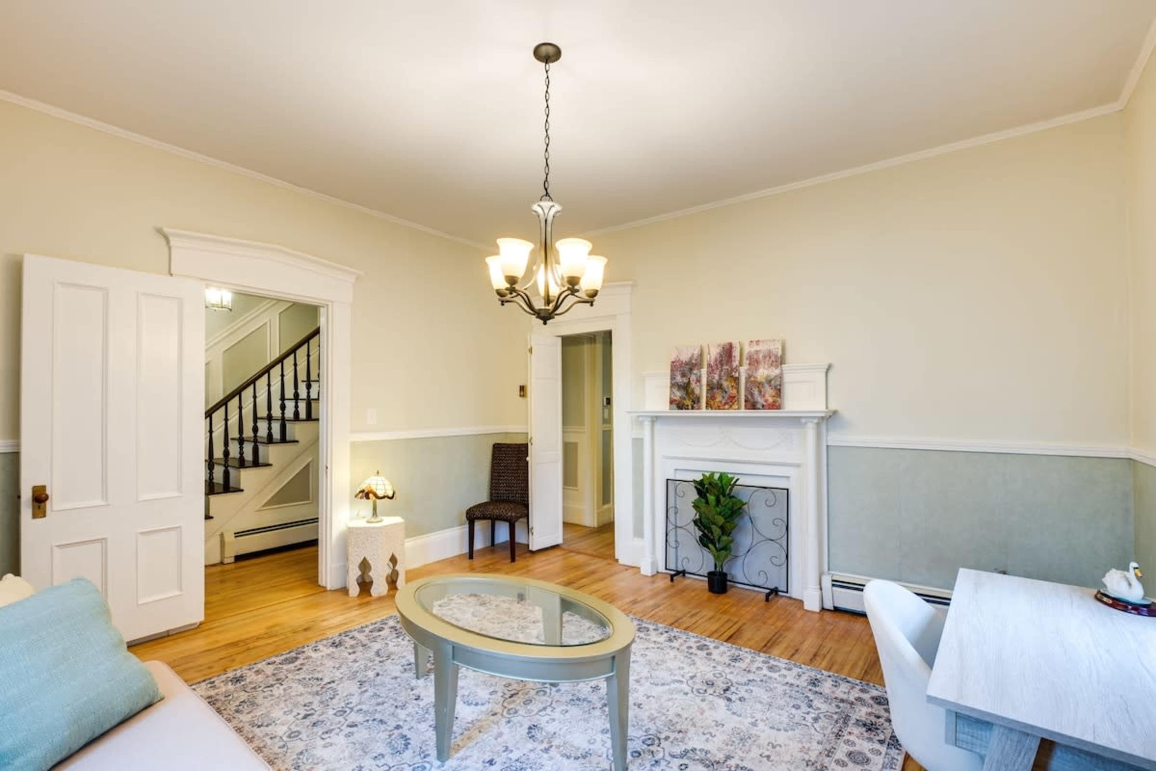 A living room with a chandelier, a fireplace, a decorative table, and a view of an adjoining staircase.