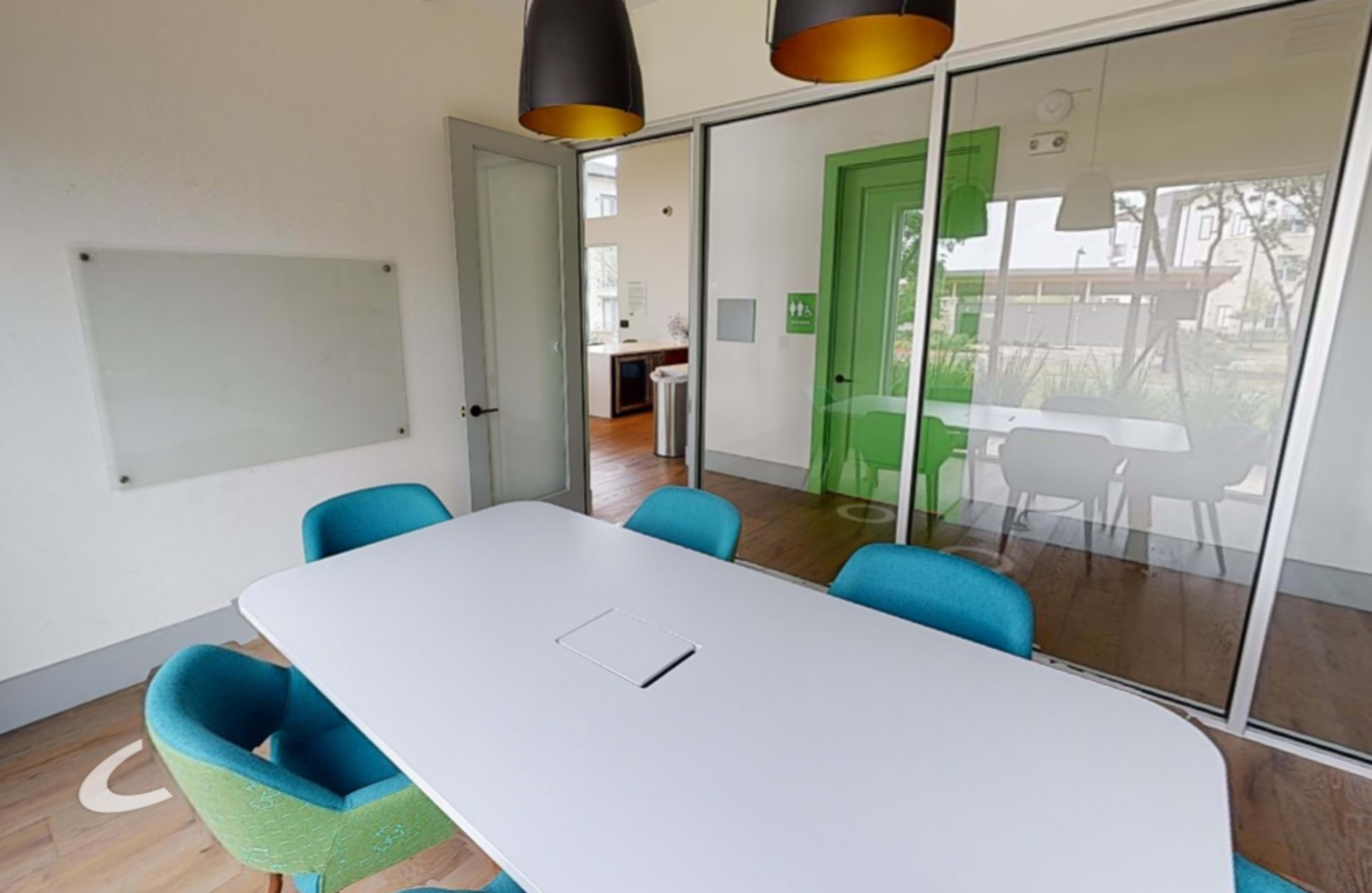 A modern conference room features a large white table surrounded by teal chairs, with glass walls and a vibrant green door in the background.