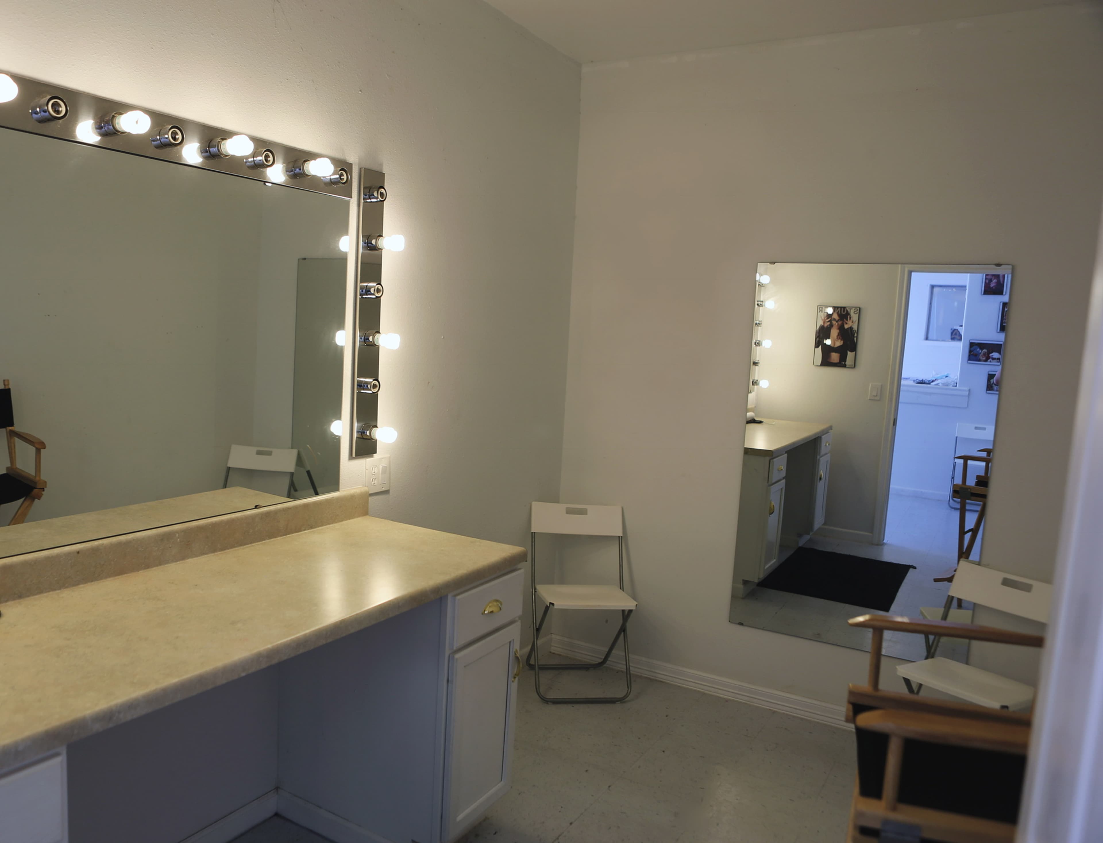 A well-lit dressing room with two mirrors, a countertop, and two folding chairs.