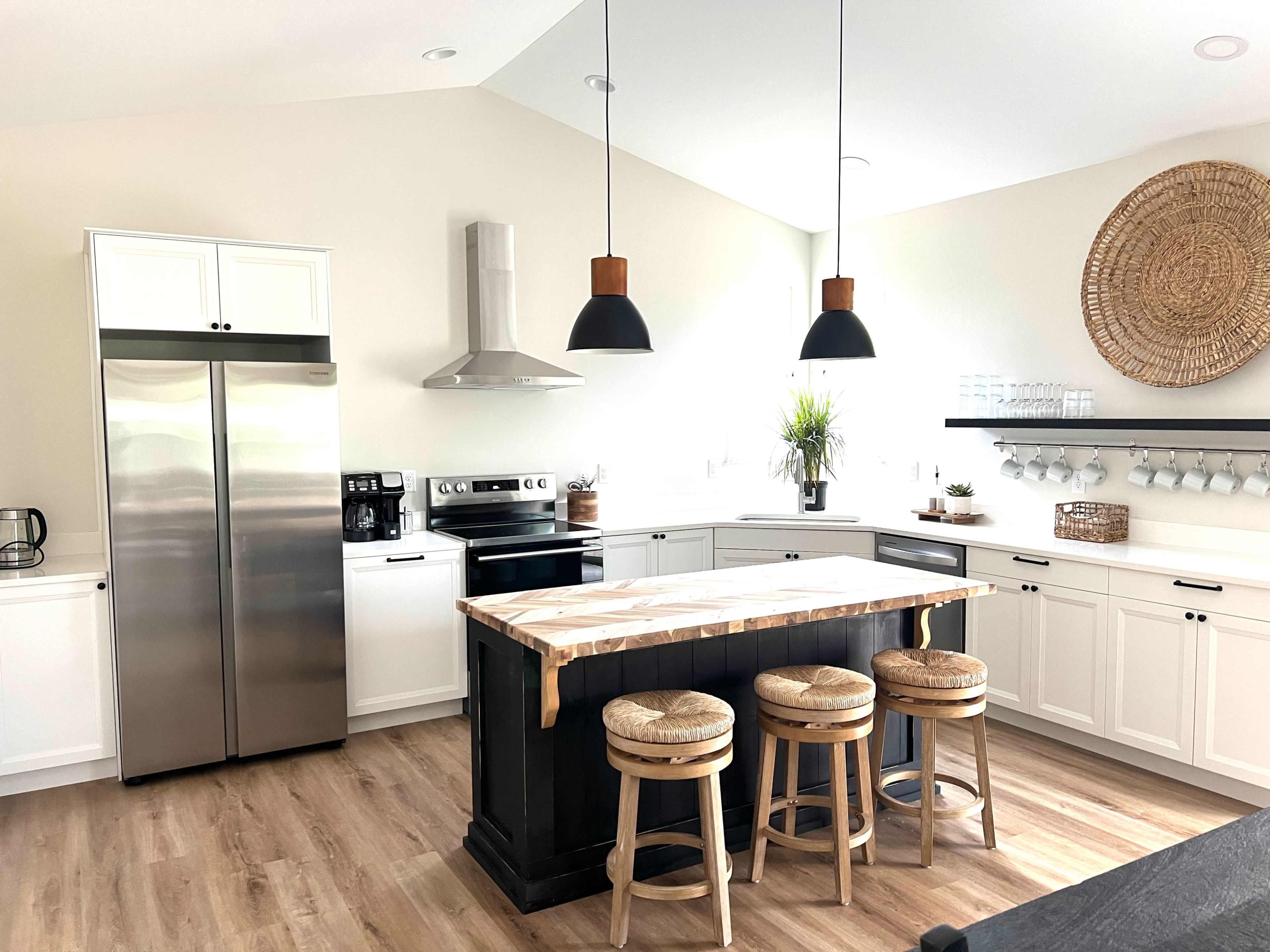 The image shows a modern kitchen featuring stainless steel appliances, a central island with a wooden countertop, and three stools.