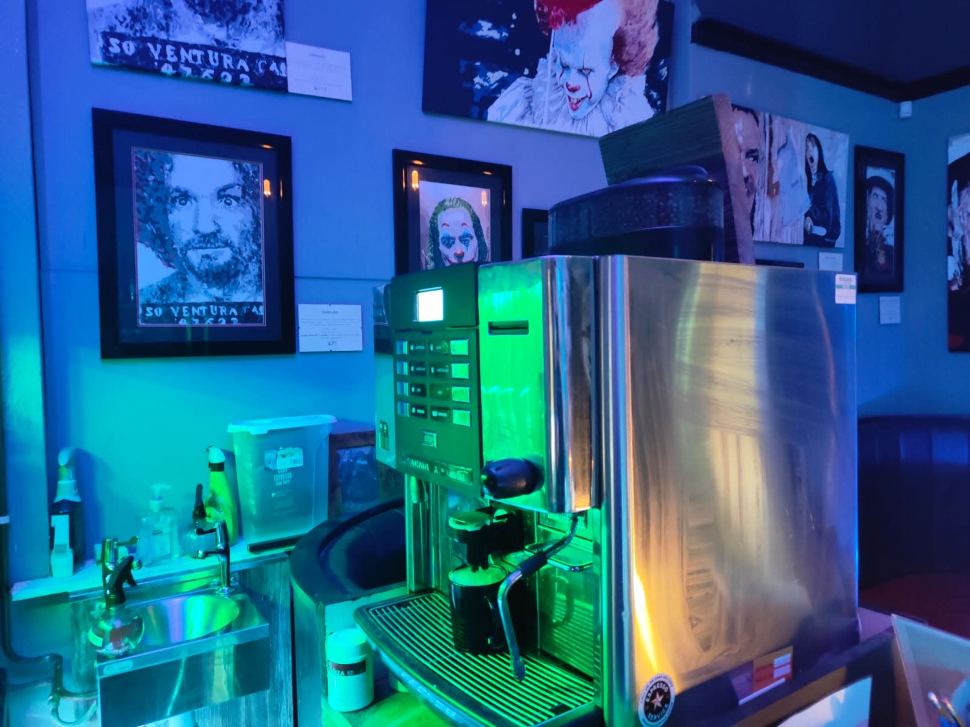 A coffee machine prominently featured in a dimly lit cafe adorned with framed portraits on the walls.