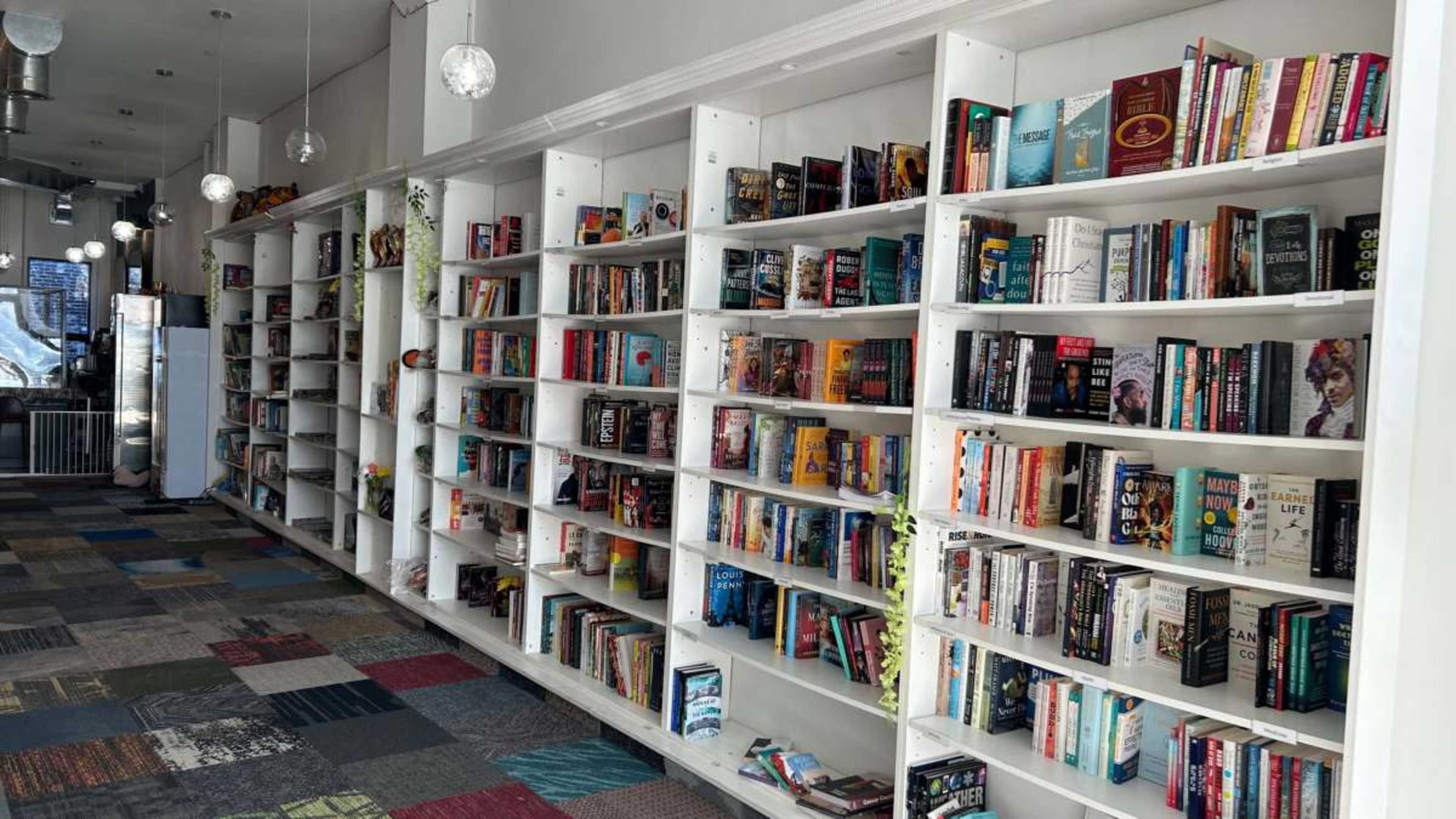 A row of white bookshelves filled with various books in a brightly lit bookstore with a tiled floor.