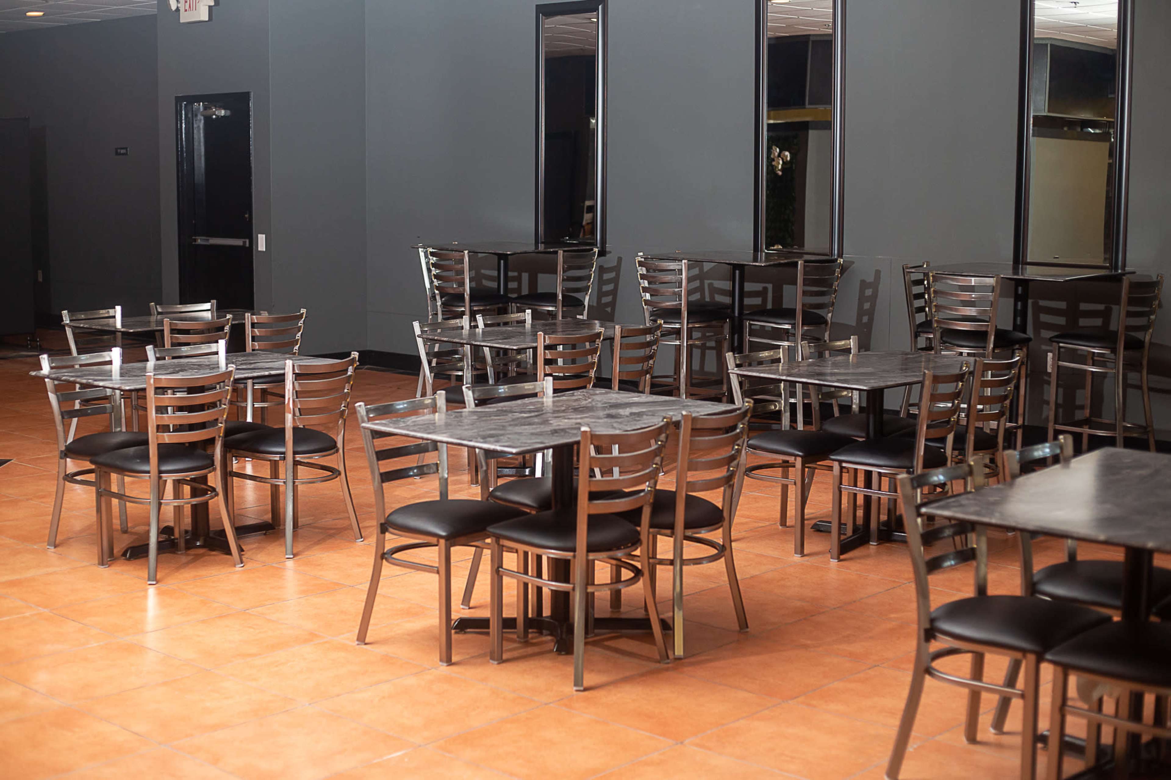 The image shows a spacious dining area with several metal-framed tables and chairs arranged on a tiled floor.