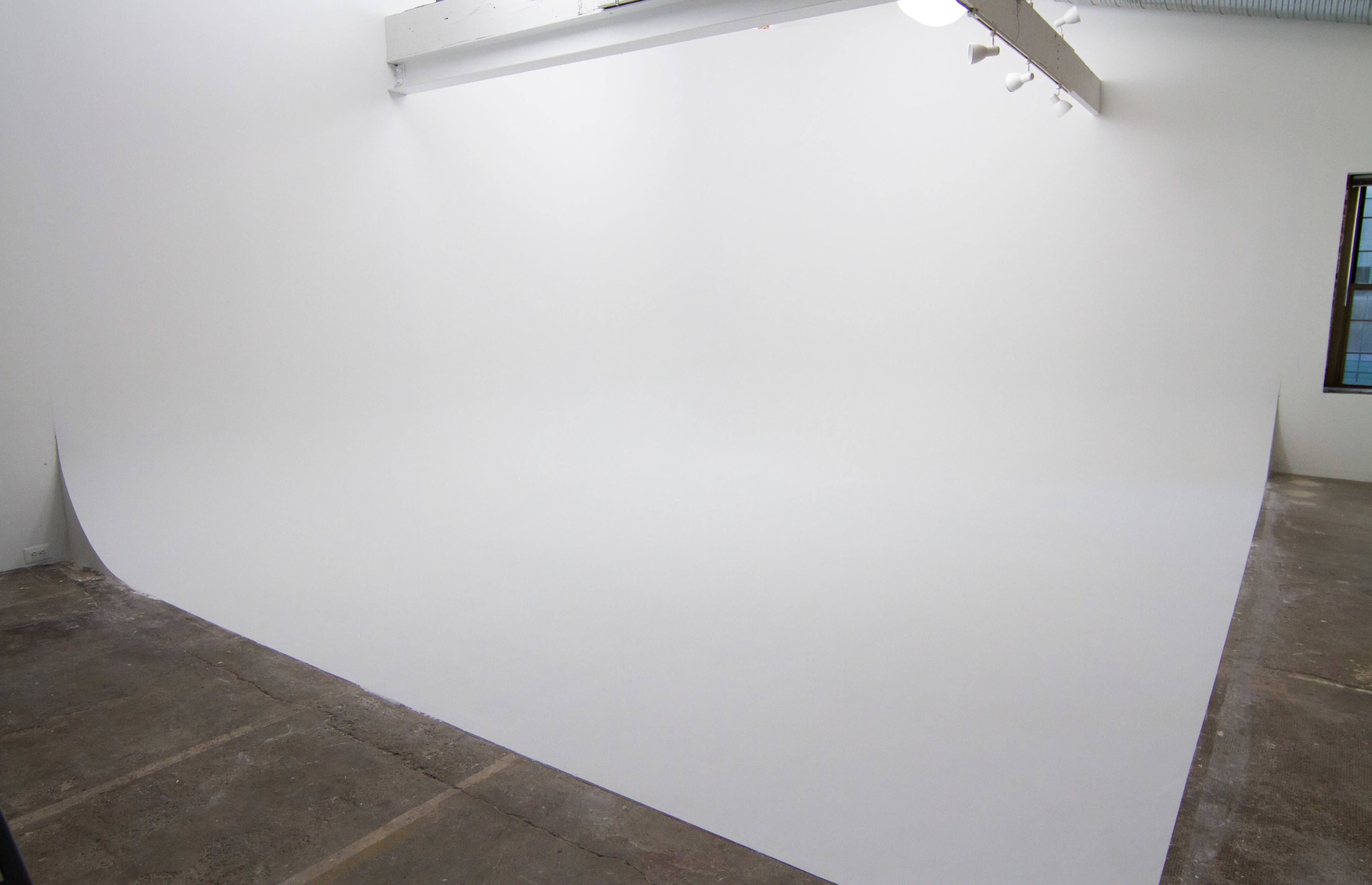 A spacious studio with a seamless white backdrop and concrete flooring.